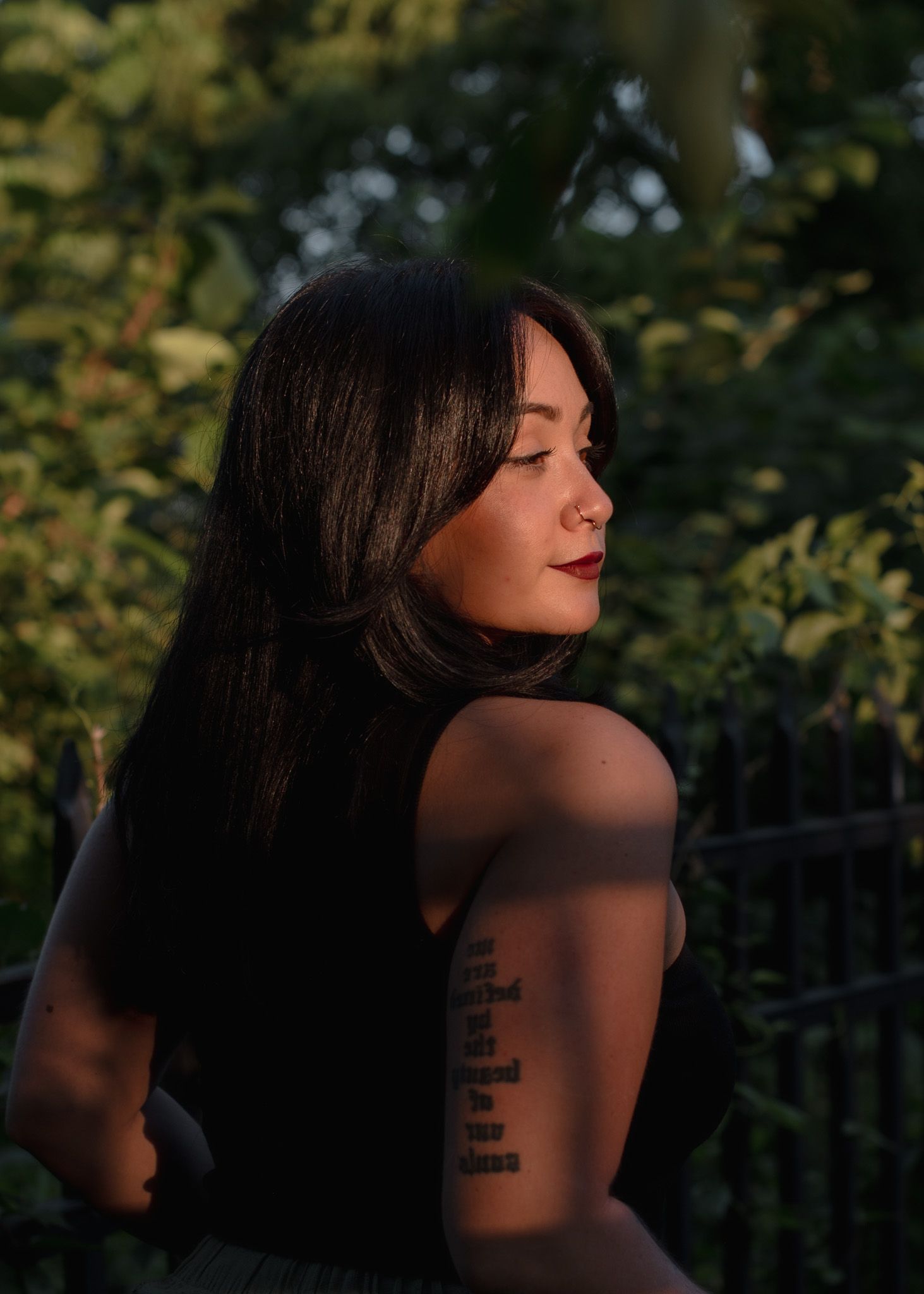 Artistic portrait of a woman with dark hair in natural lighting showing tattoos.