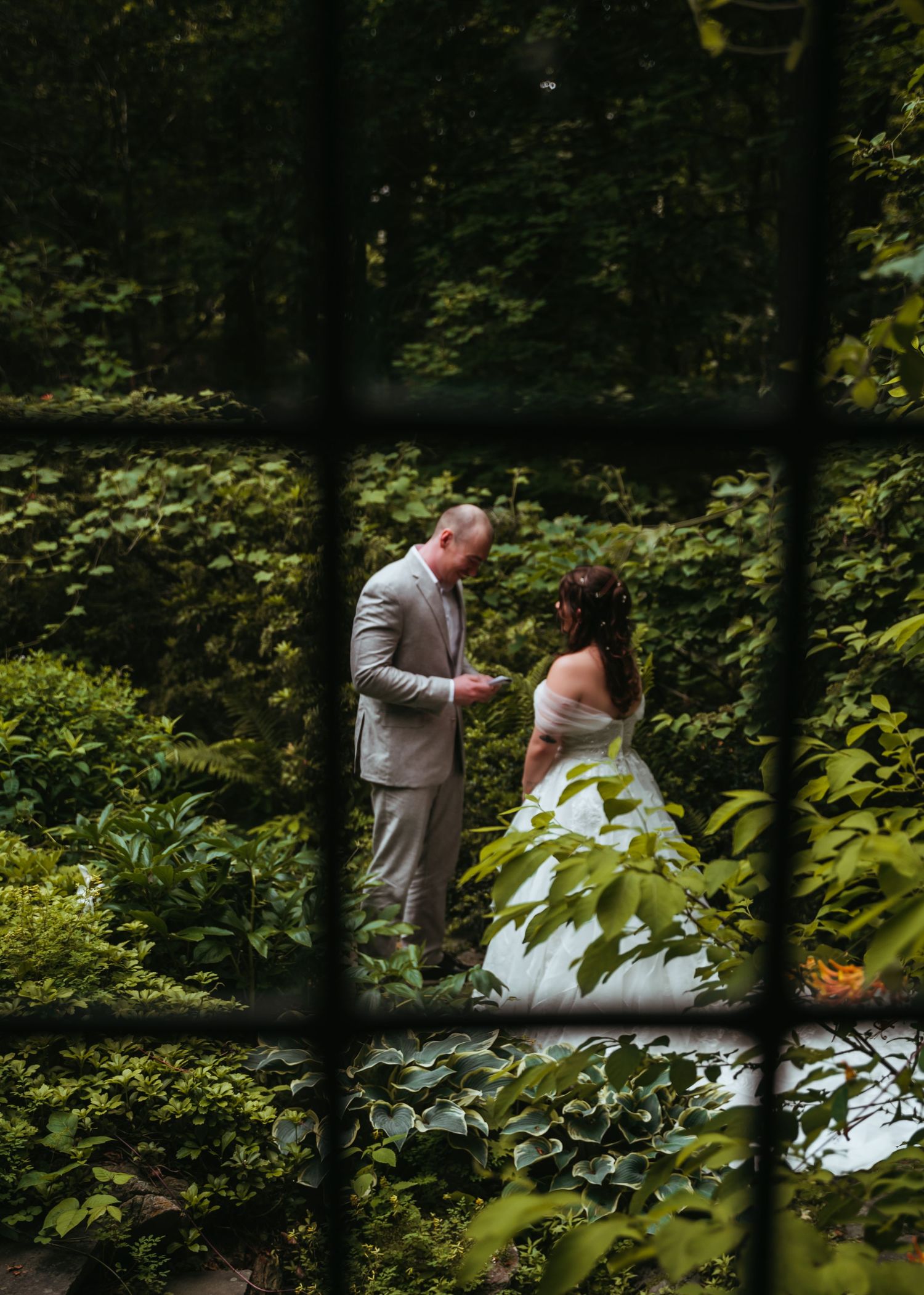 A couple shares a romantic moment in a lush garden setting framed by green foliage and natural light.