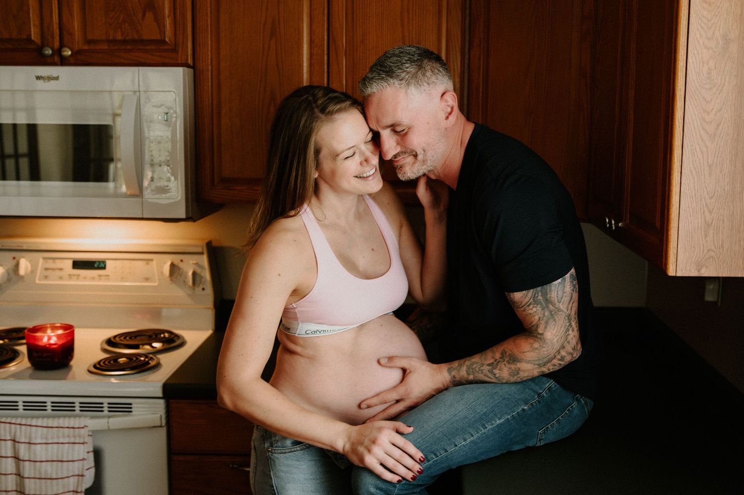 Couple shares intimate moments in cozy kitchen setting with warm lighting and rustic wood cabinetry.