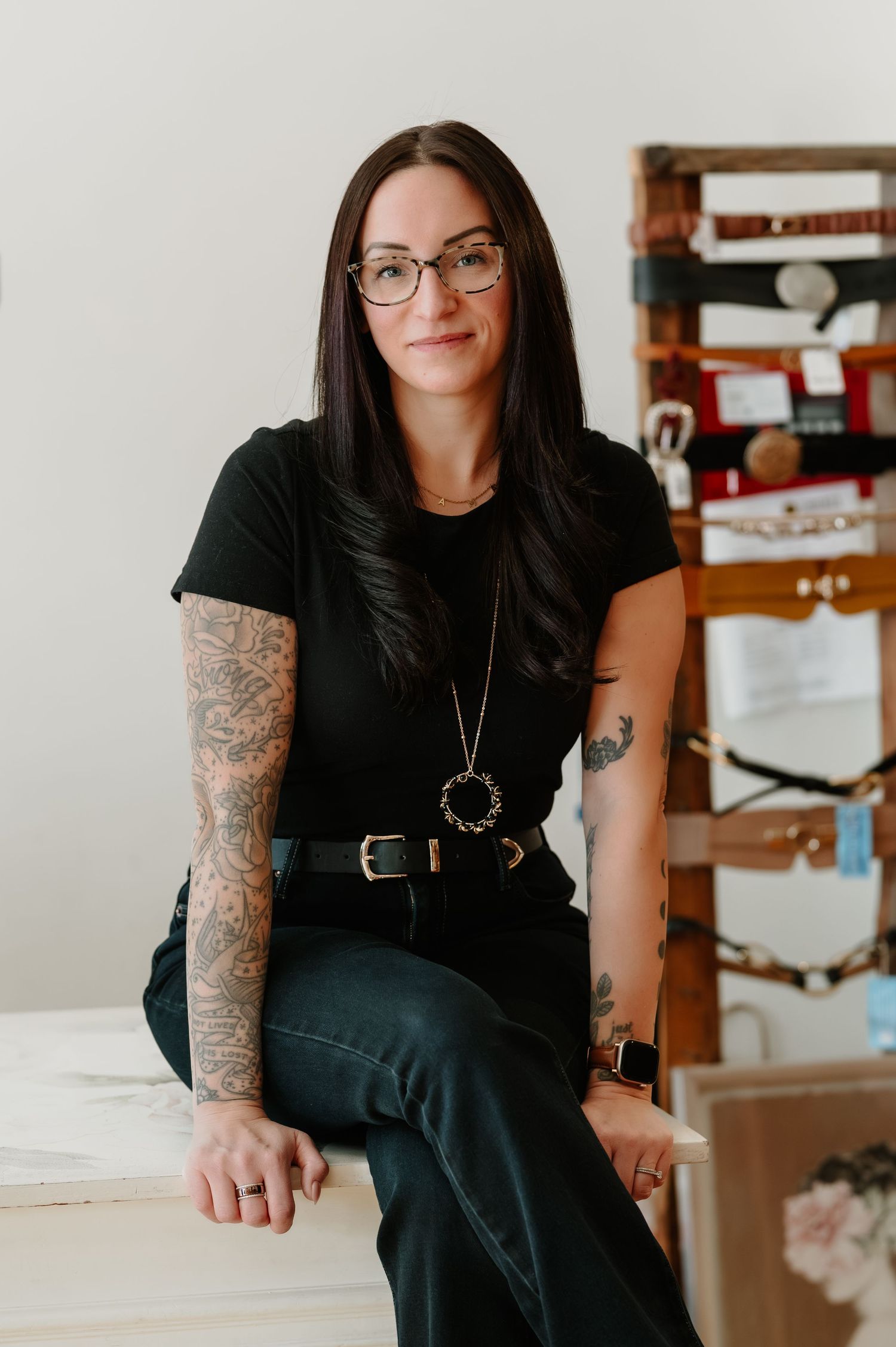 Woman in black outfit with tattoo sleeve sitting in minimalist interior setting.