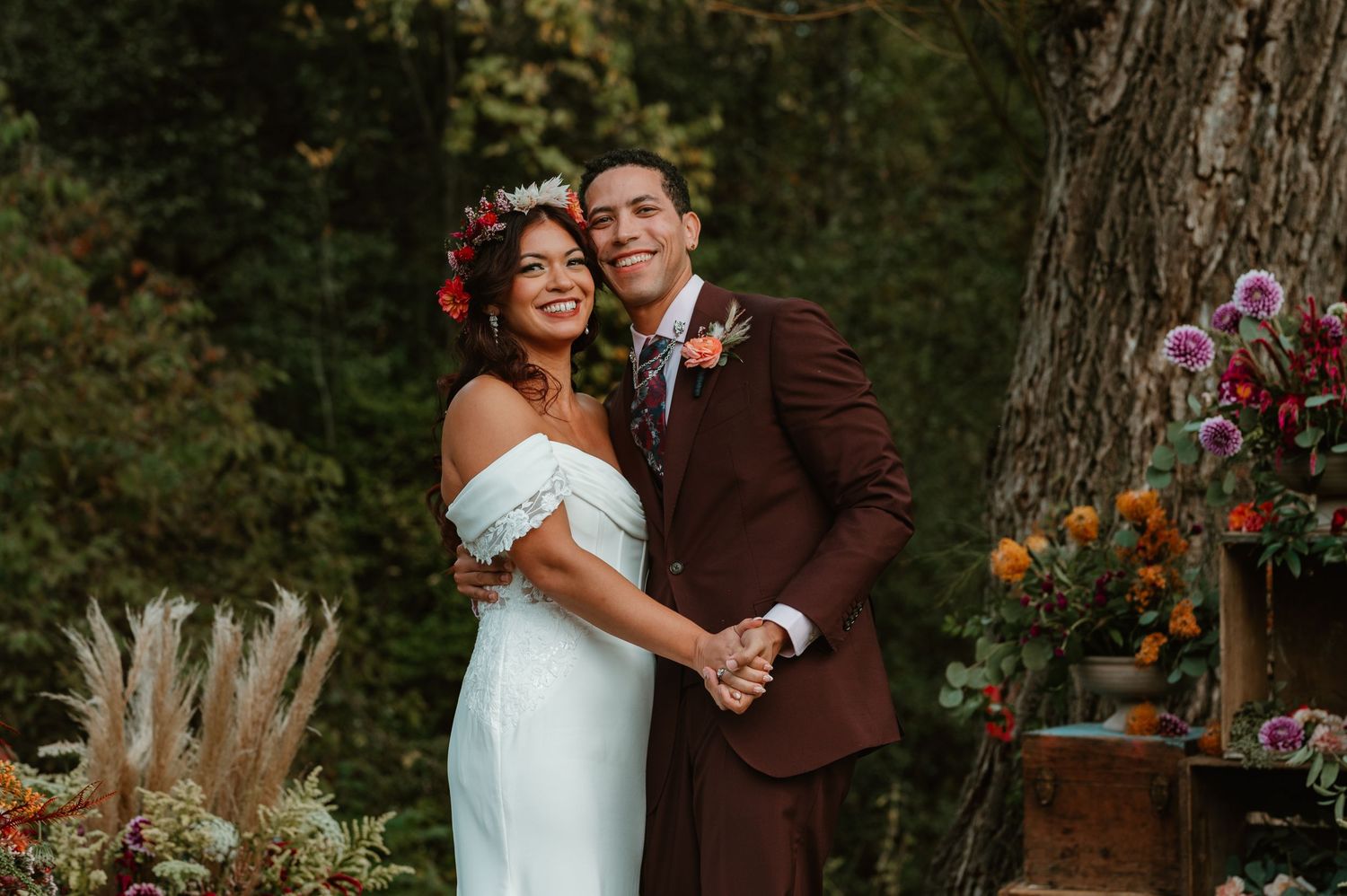 Wedding couple embraces outdoors against backdrop of autumn trees and natural foliage.