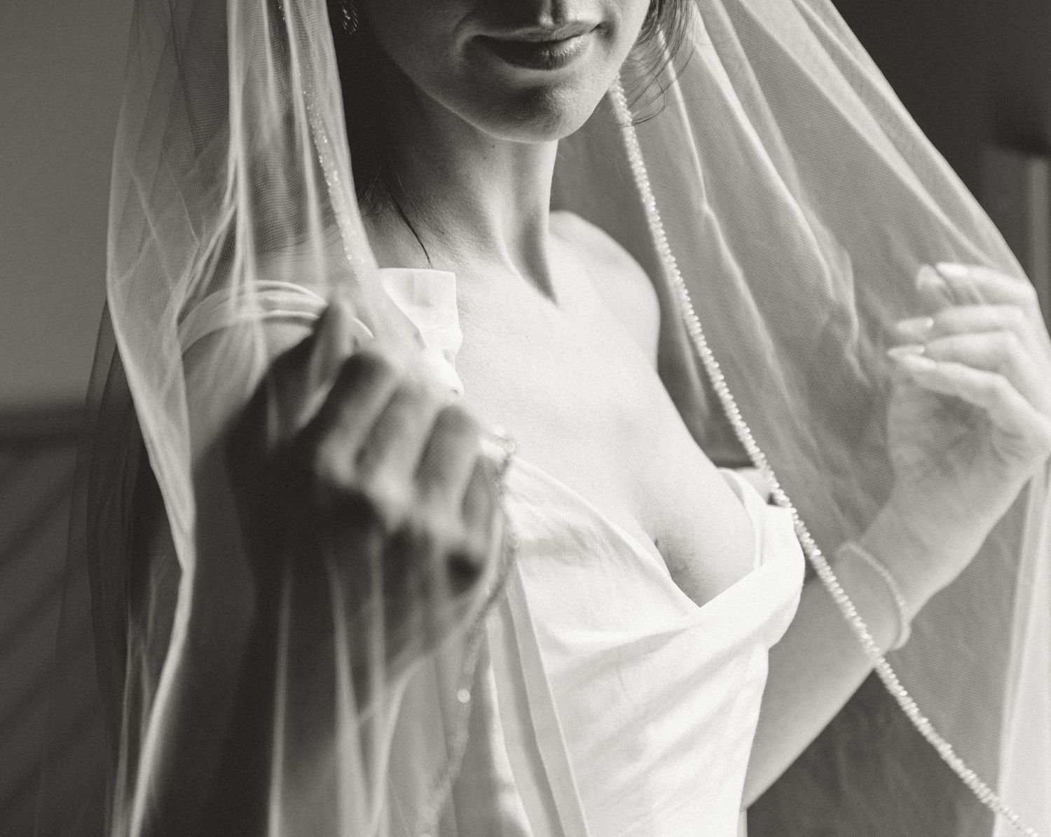 A black and white close-up photograph showing a delicate bridal veil and white wedding dress.