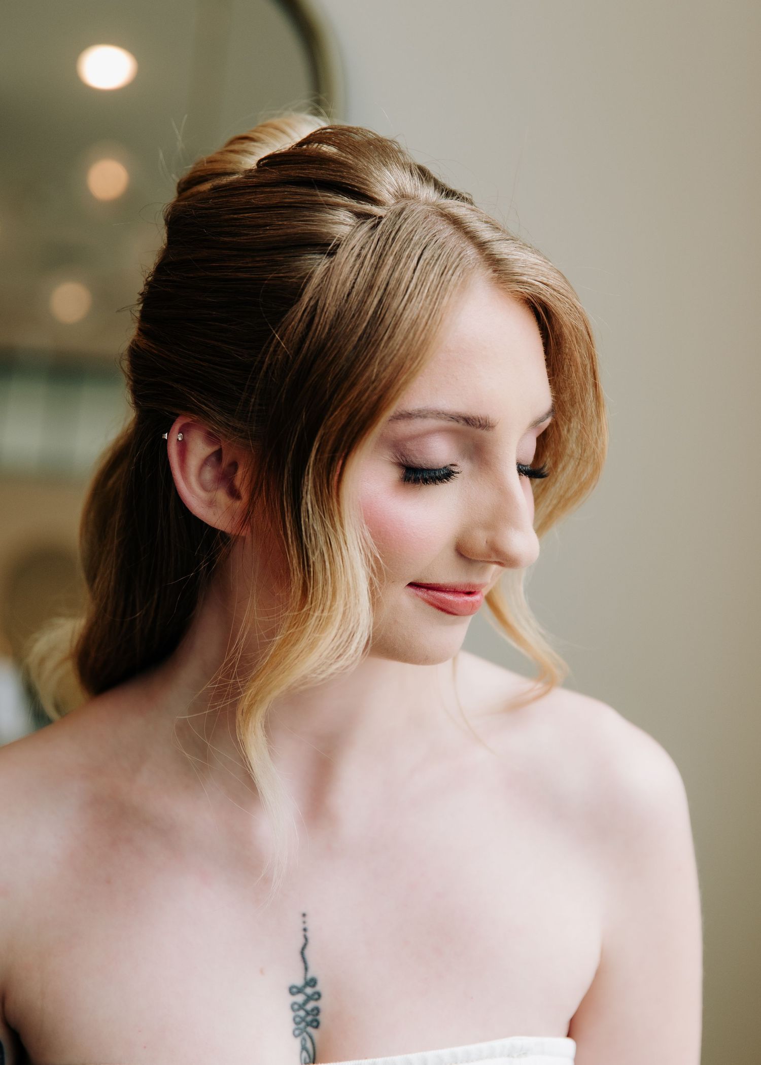 Elegant bridal updo hairstyle with soft waves and natural makeup on a young woman in a strapless dress.