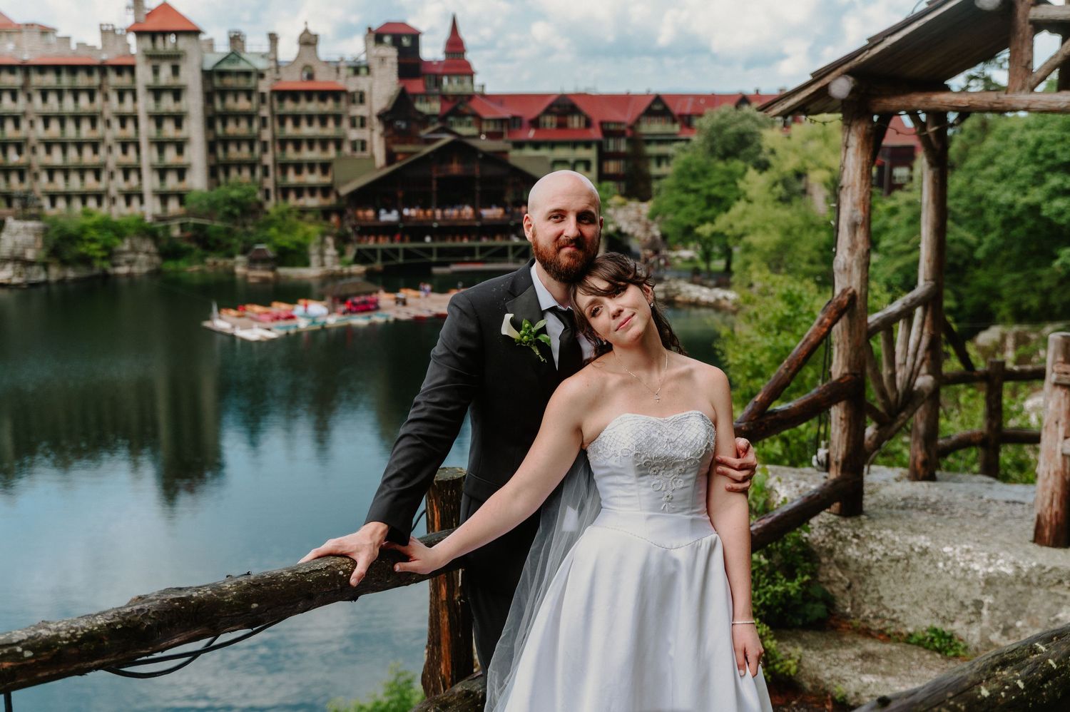 Bride and groom posing on a wooden bridge overlooking a lake at Mohonk Mountain House wedding venue.