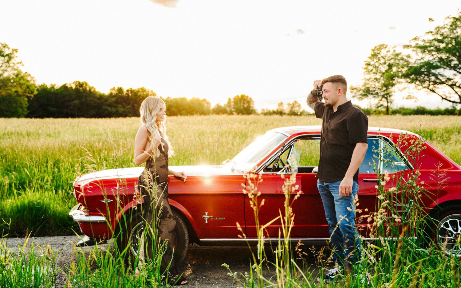 Romantic countryside engagement photos with a classic red car at sunset.