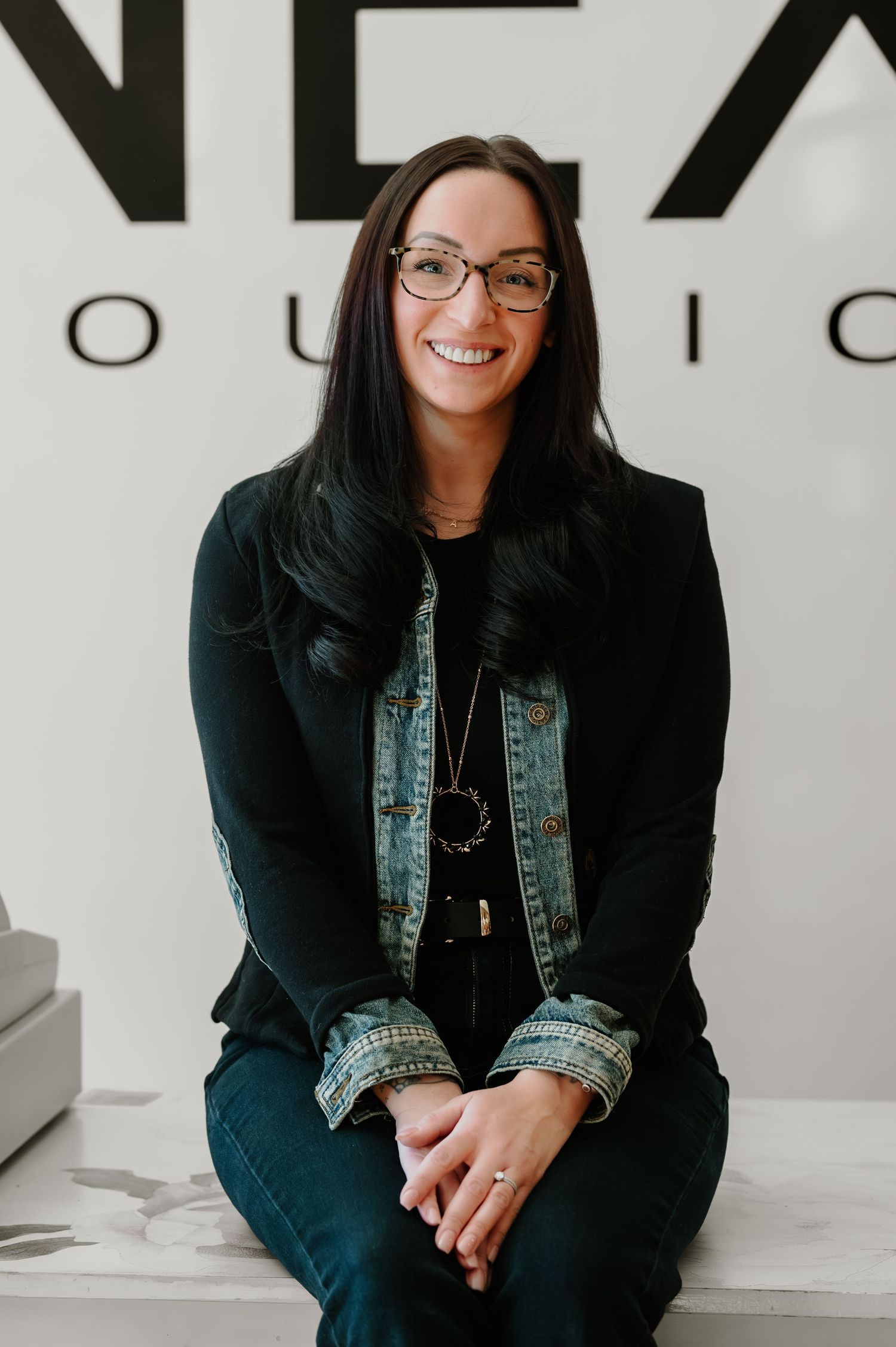 Professional portrait series showing a person in a black blazer and denim vest sitting against a white background.