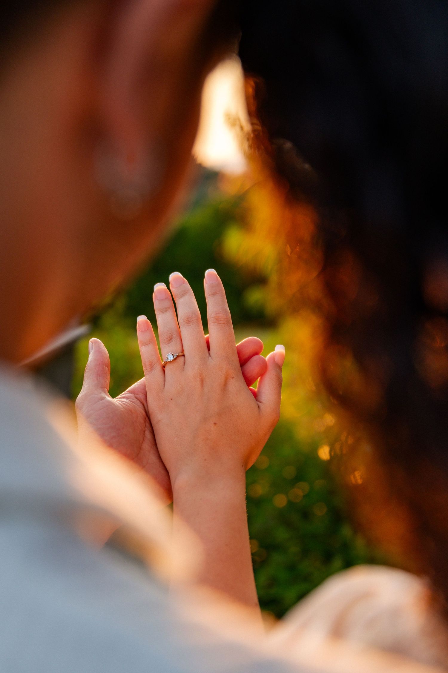 Couple admiring an engagement ring on the woman's hand outdoors in golden sunlight.