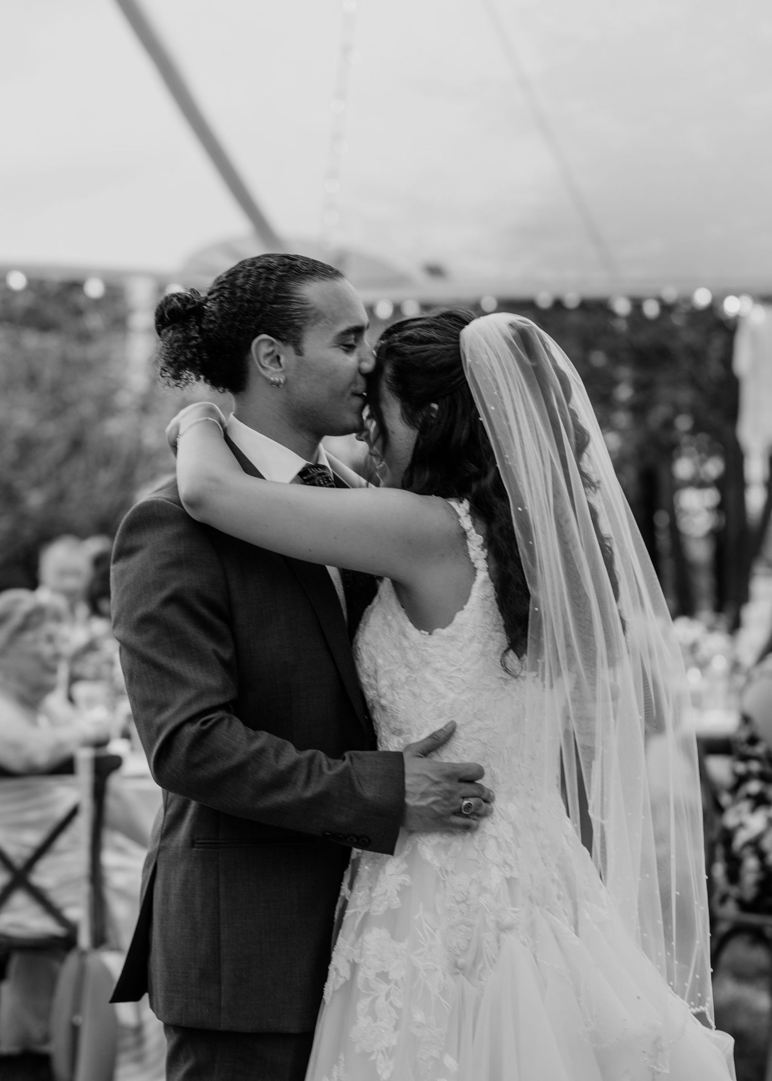 Black and white photo of a couple sharing their first dance kiss at a wedding reception under a tent.