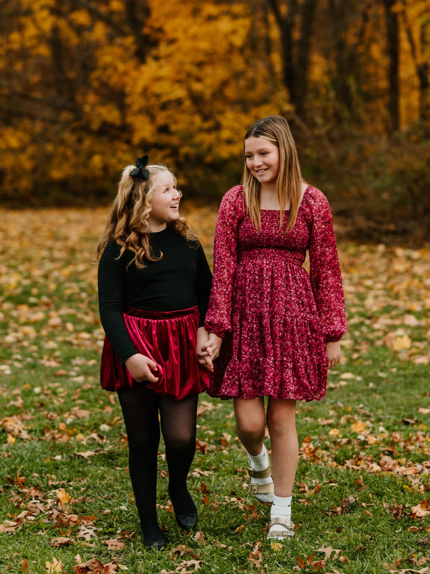 Two people in coordinating outfits share a sweet moment on fallen autumn leaves in a park setting.