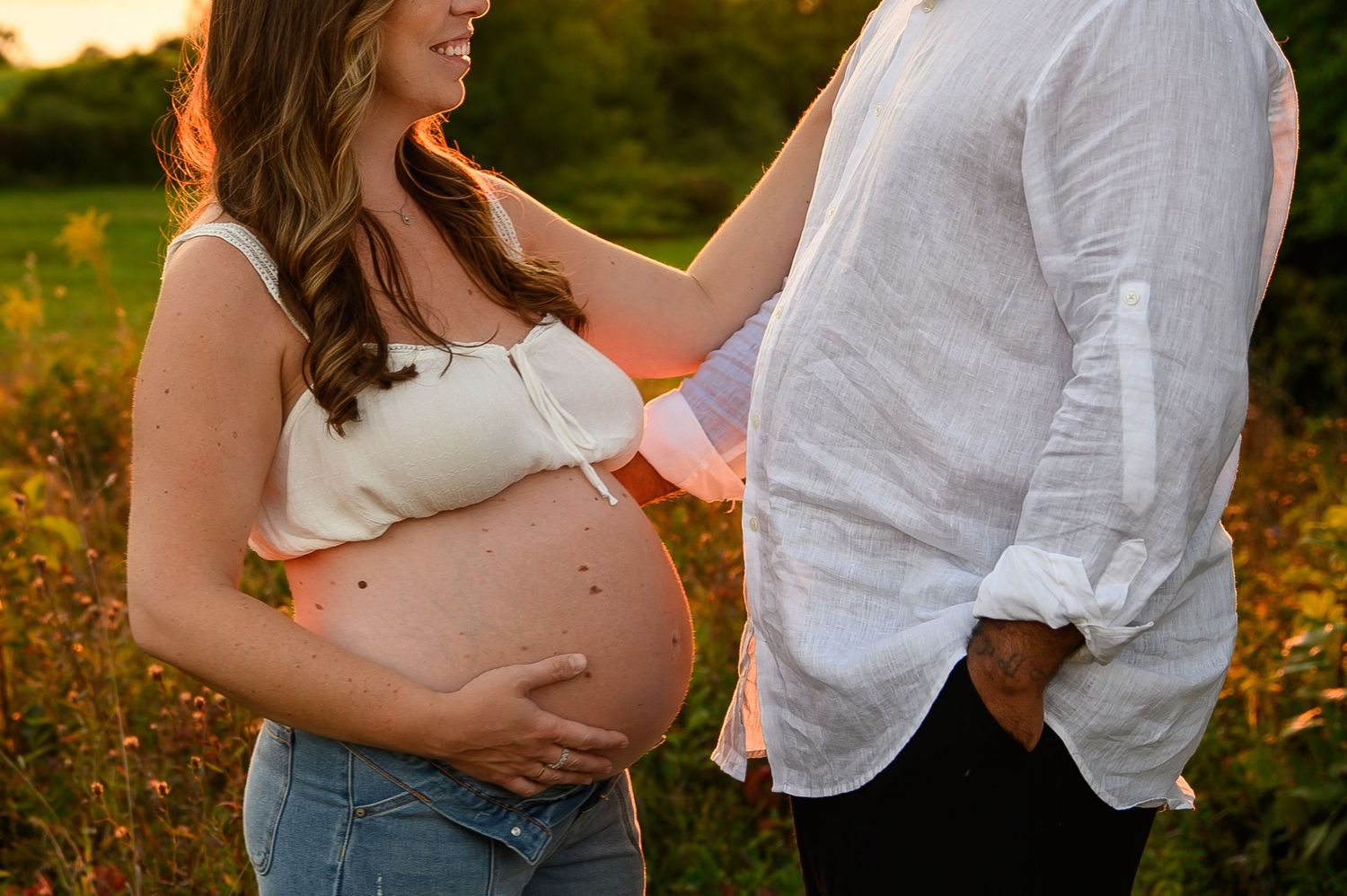 Expecting couple shares intimate moment in golden sunlit field during maternity photoshoot.