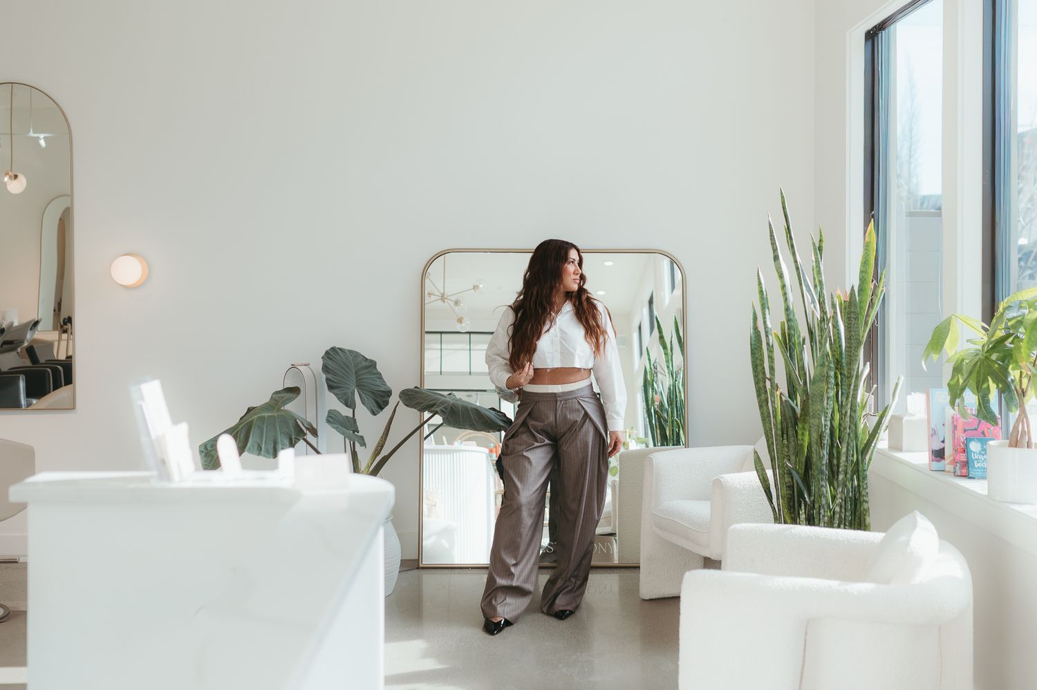 A bright modern office interior with white walls, potted plants, and natural lighting through large windows.