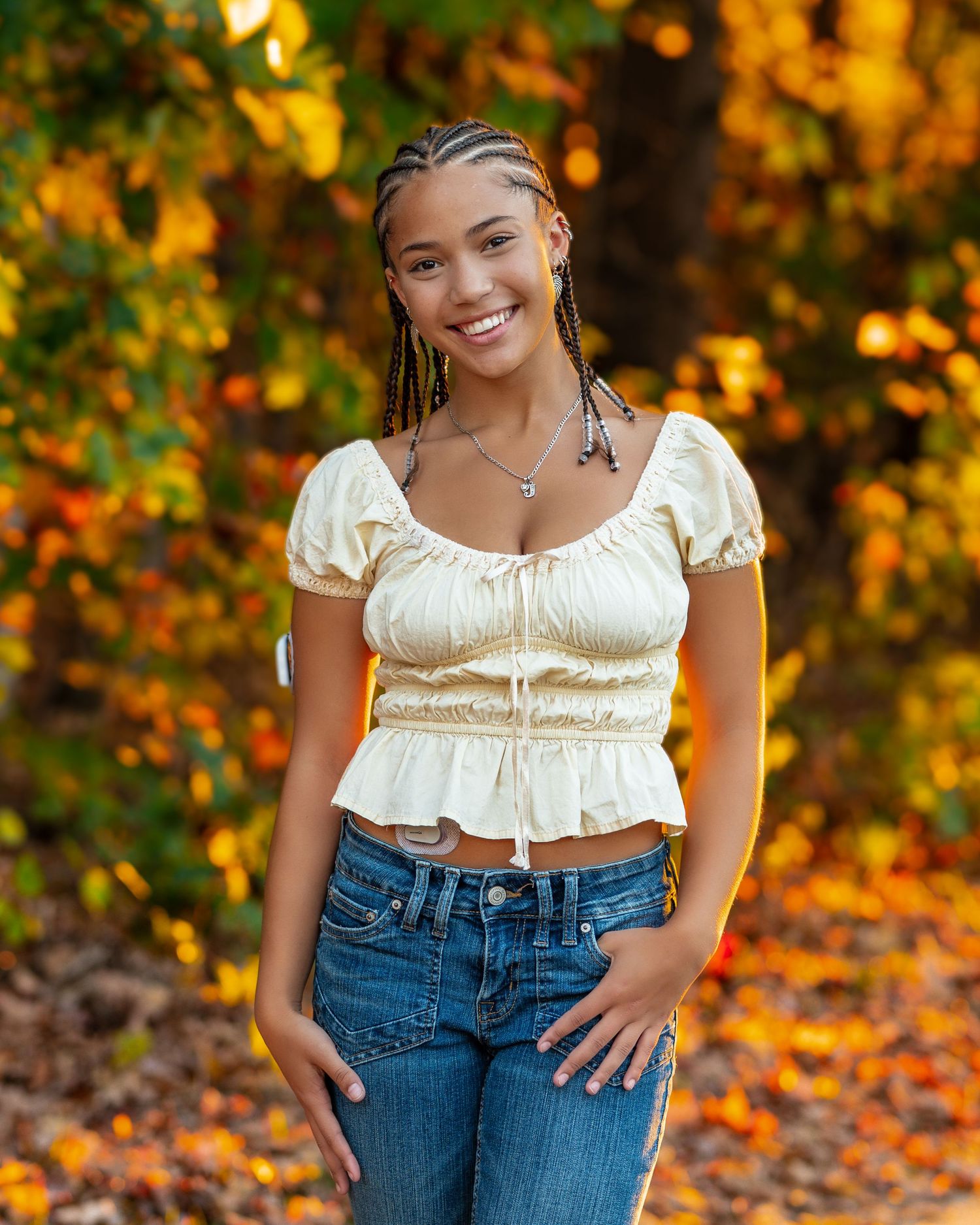 Outdoor portrait with cornrow braids wearing white ruched crop top against fall colors.
