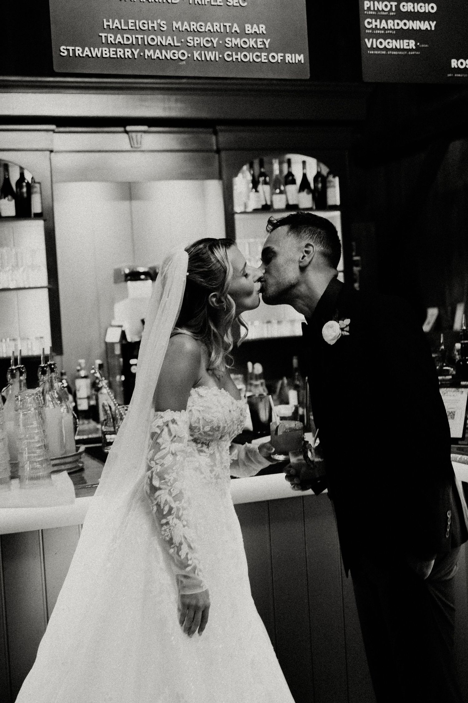Black and white photo series of a romantic moment between a couple in formal wedding attire at a bar counter.