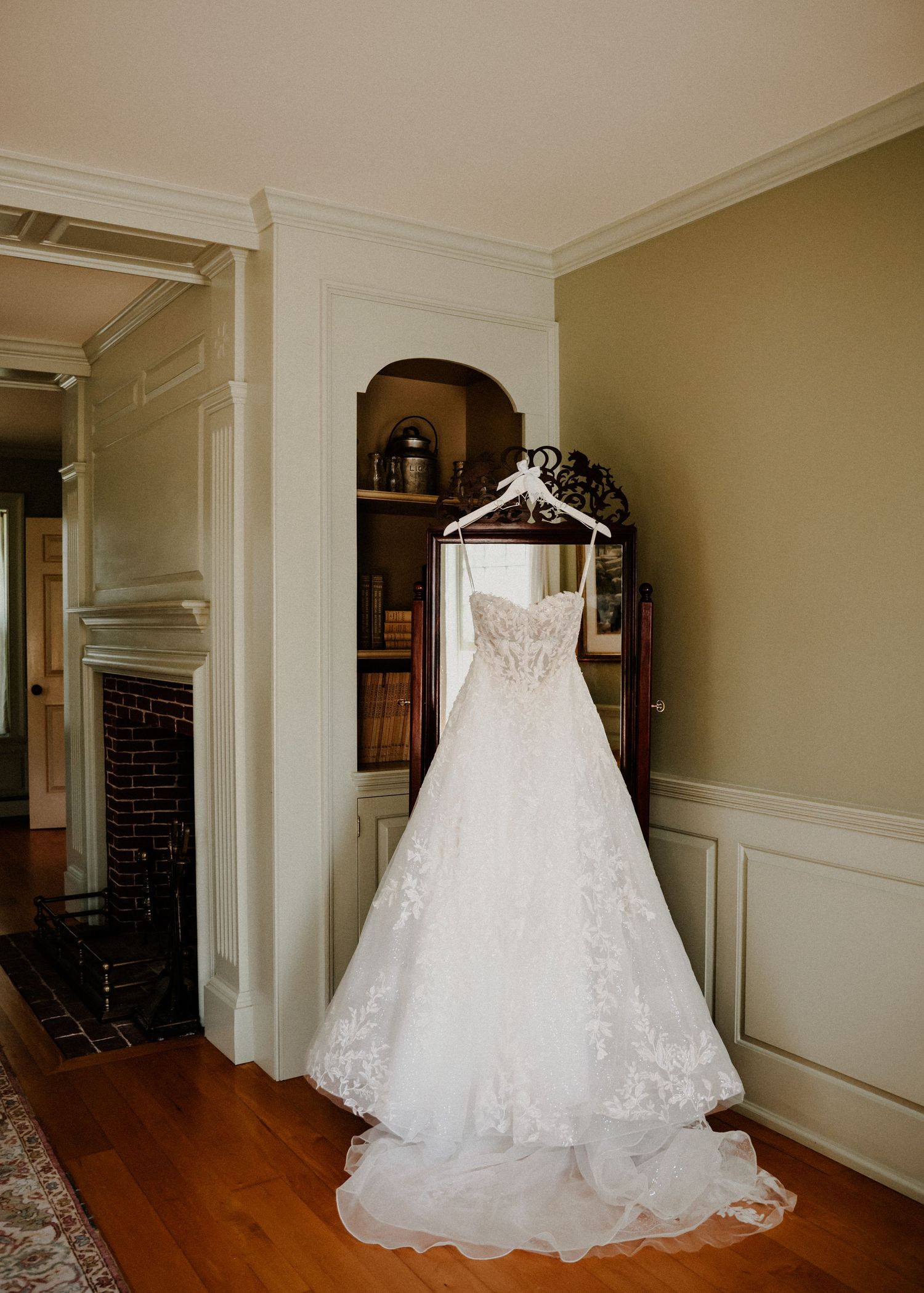 A sequence of white wedding dresses displayed in a hallway with hardwood floors and cream-colored walls.