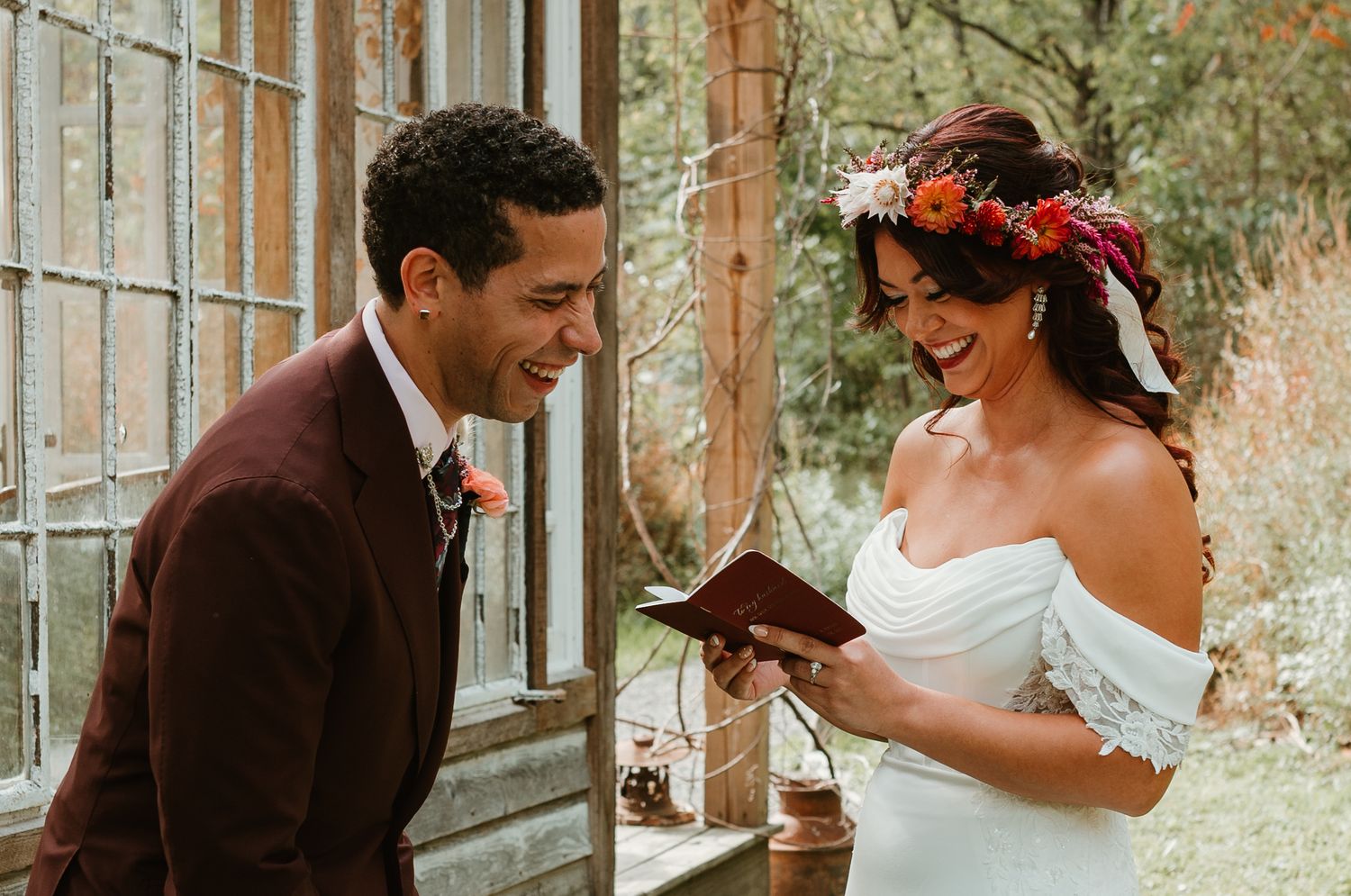 A couple in wedding attire shares a romantic moment in front of tall glass windows at their wedding celebration.