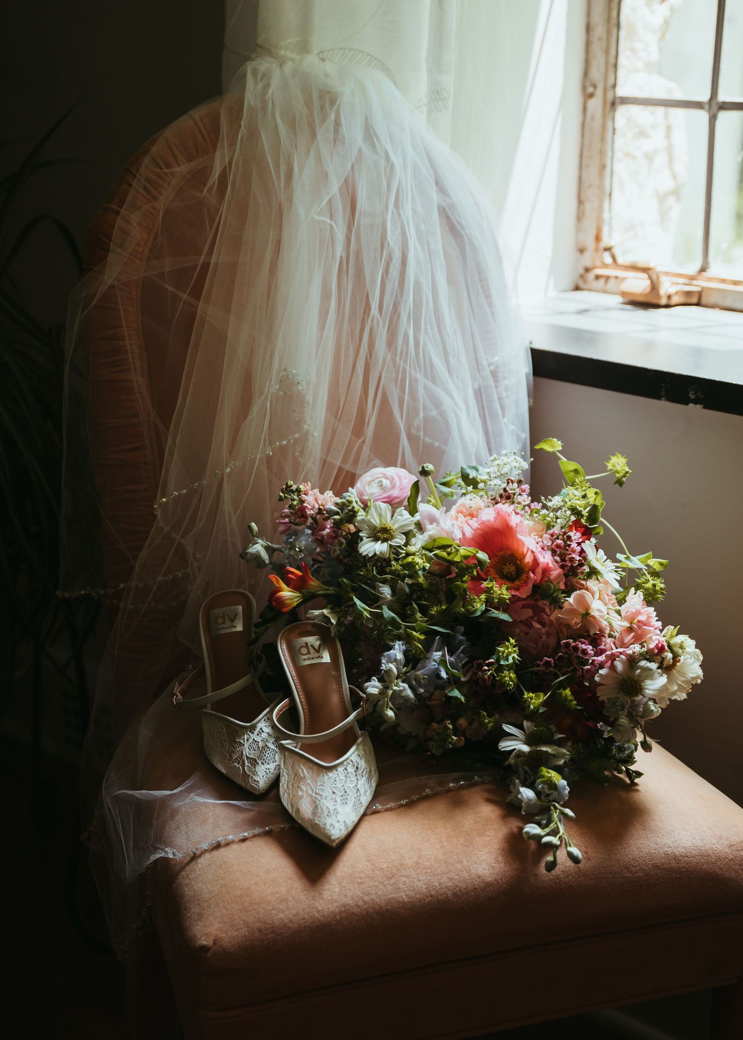 Wedding details with floral arrangements and tulle veil displayed on rustic windowsill.