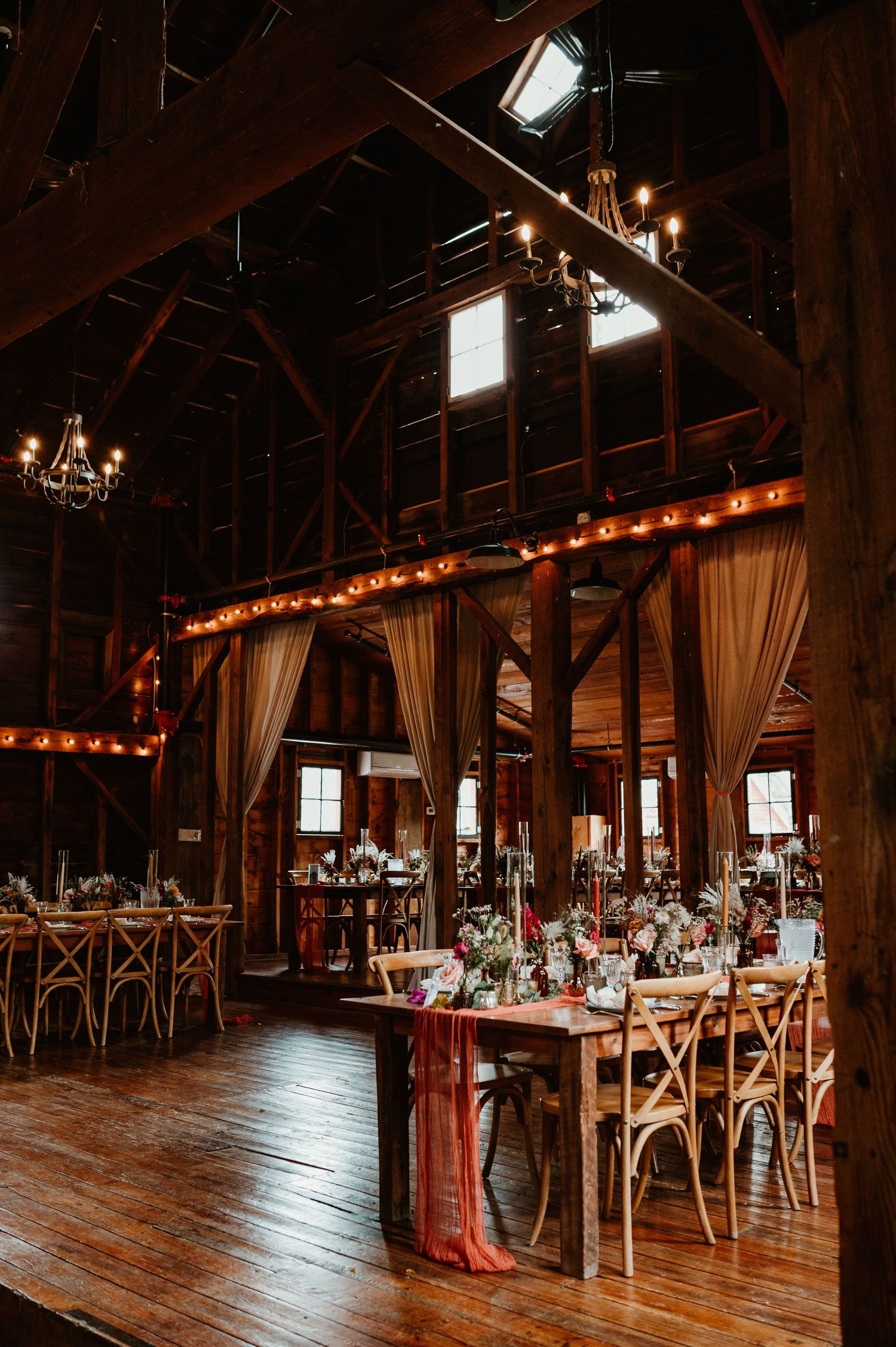 Rustic barn venue interior with wooden beams, floors and elegant lighting setup for a wedding reception.