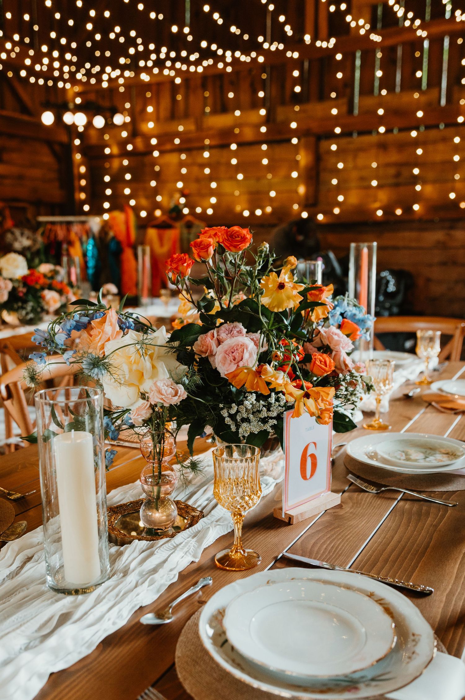 Rustic wedding reception table setting with string lights overhead and floral centerpieces in warm autumn colors.