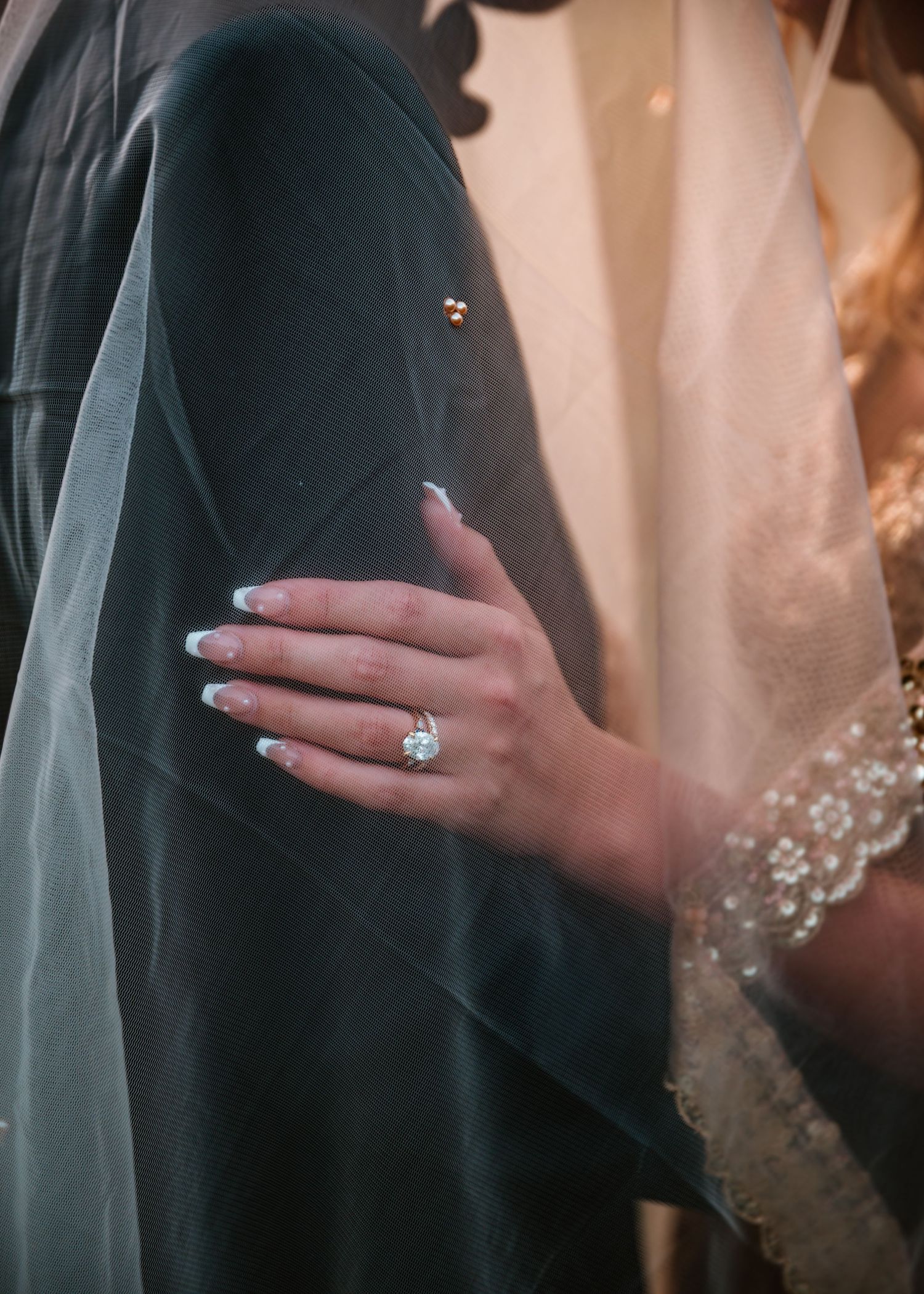 A delicate white veil and sparkling engagement ring shown in an elegant bridal detail shot.