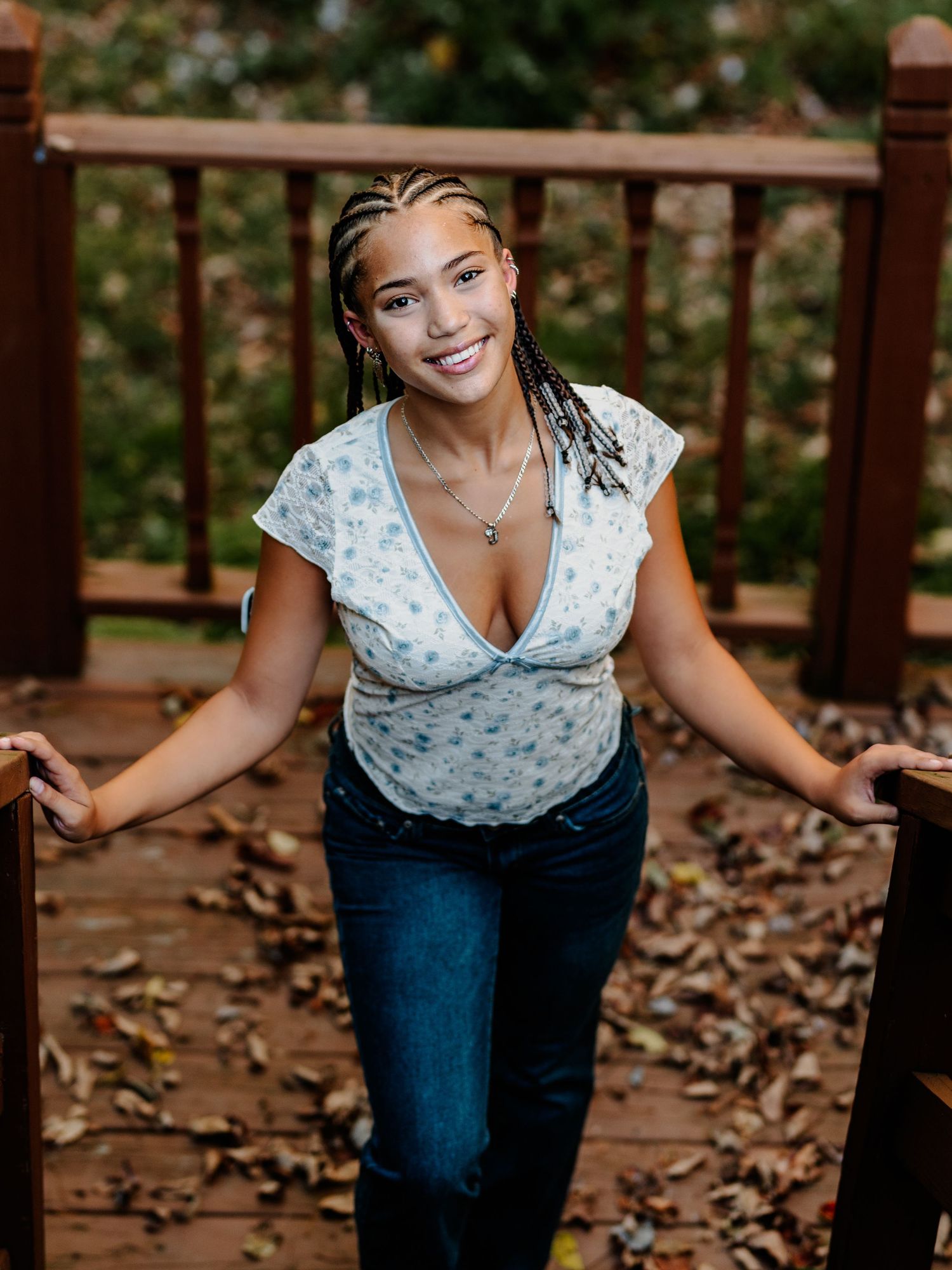 A woman in a polka dot top and jeans poses playfully on wooden steps covered with autumn leaves.