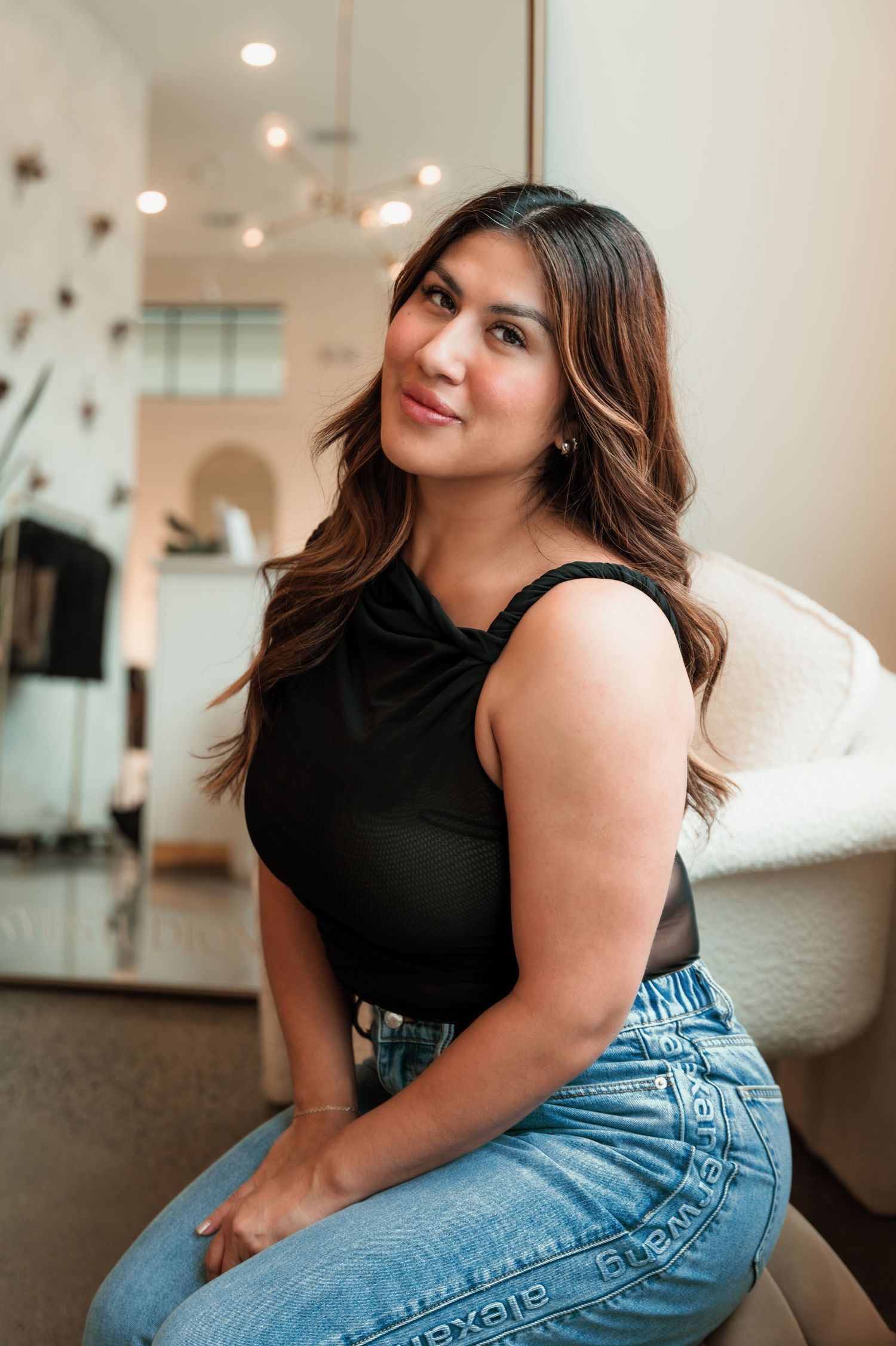 Woman in black sleeveless top and jeans sitting and smiling in a modern bright interior setting.