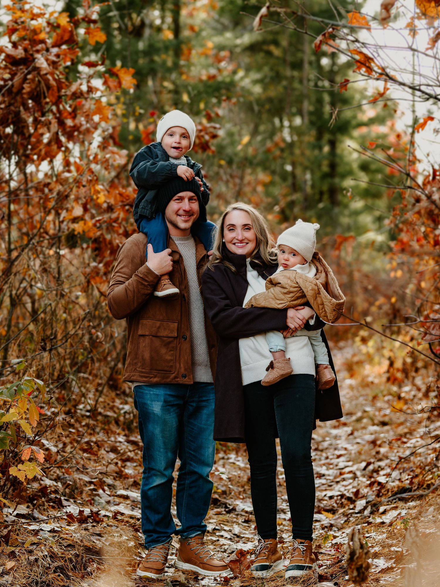 A family enjoys a playful autumn photoshoot among fallen leaves and orange foliage in a wooded setting.