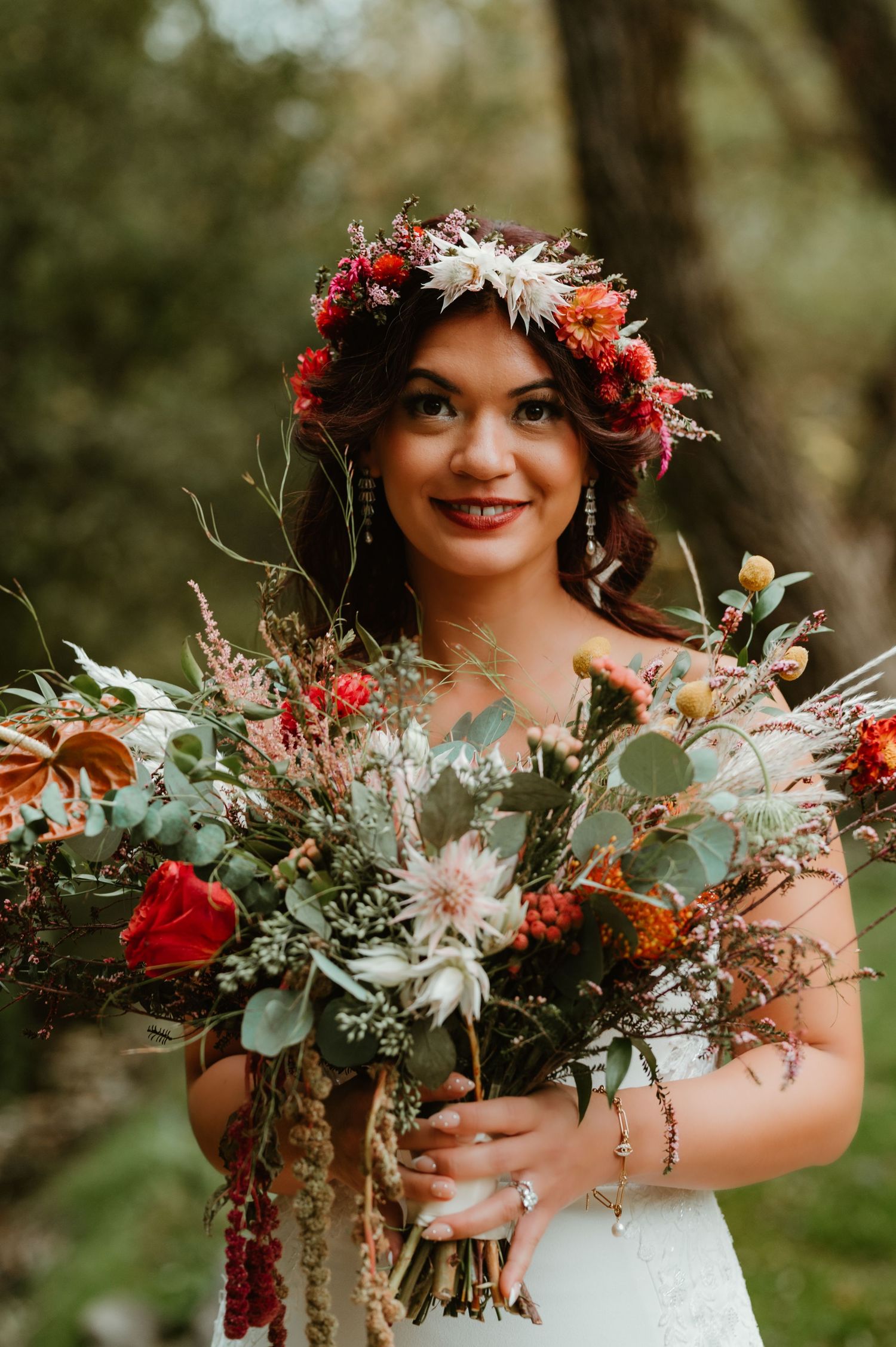 A wedding portrait showing a bouquet of red and pink flowers with greenery against a natural outdoor background.