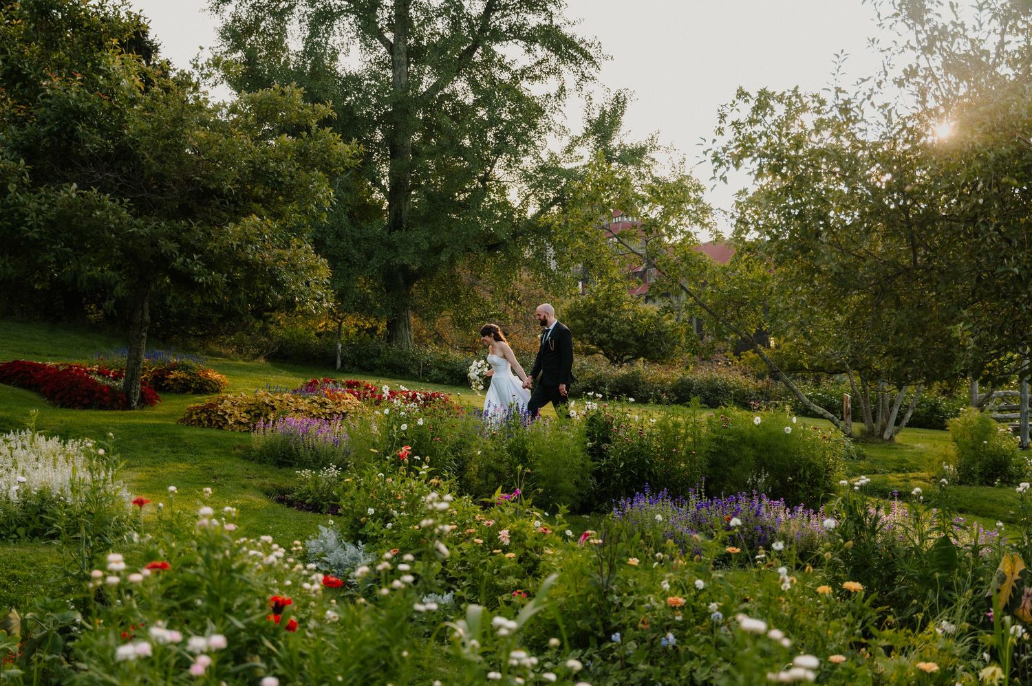 Bride and groom walking hand in hand through a lush garden filled with colorful wildflowers at golden hour.