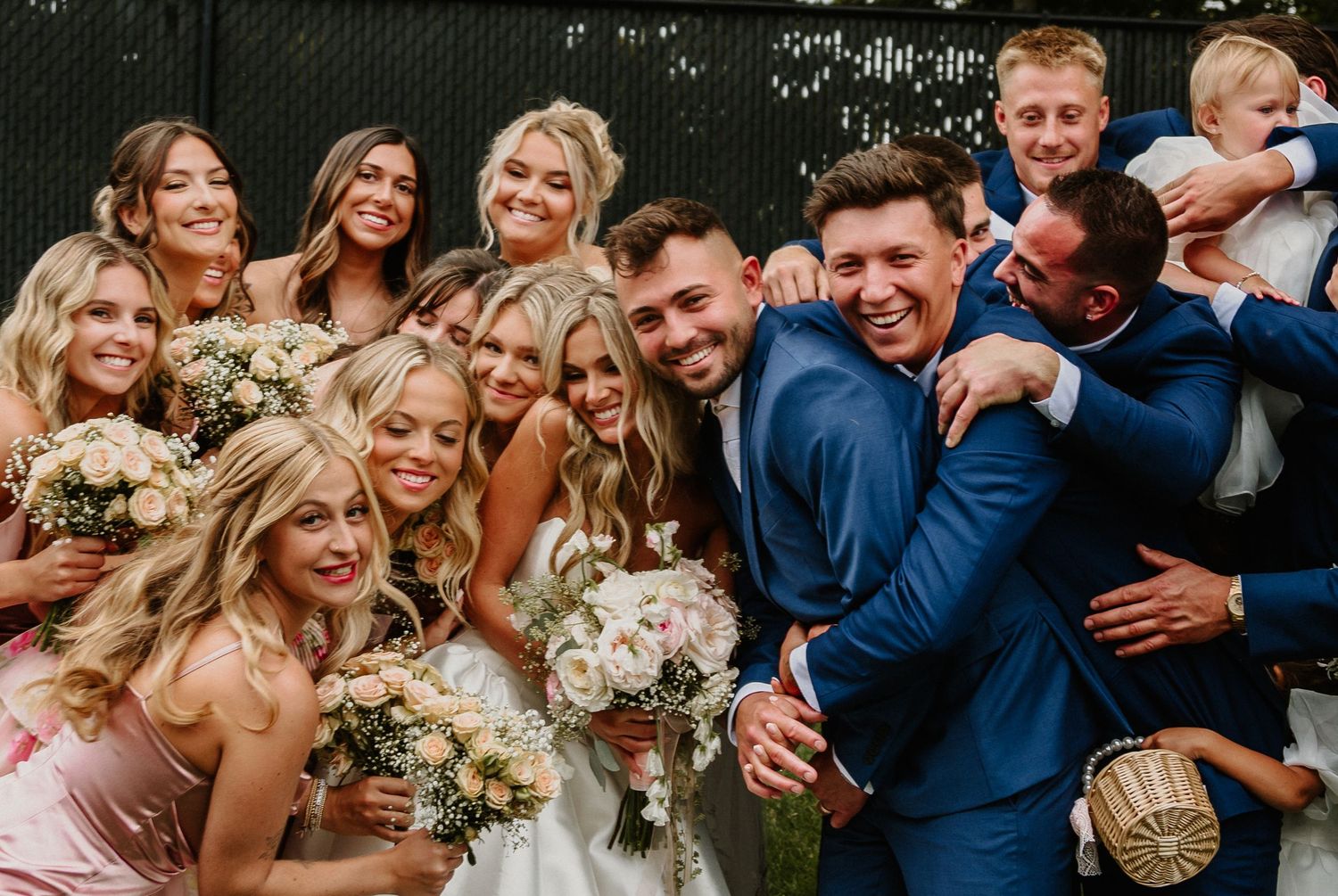 Wedding party members laugh and embrace during candid moments at an outdoor celebration.