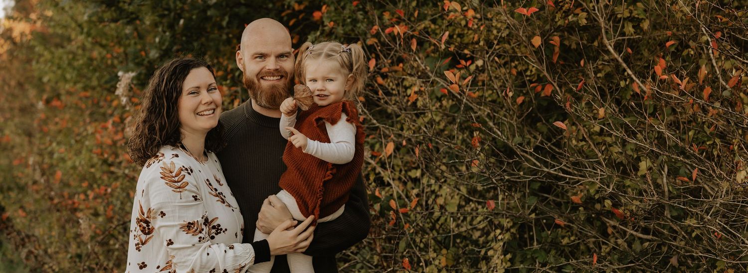 Familiefotograf i Aalborg og Nordjylland – naturligt portræt af mor, far og datter i efterårets varme farver.