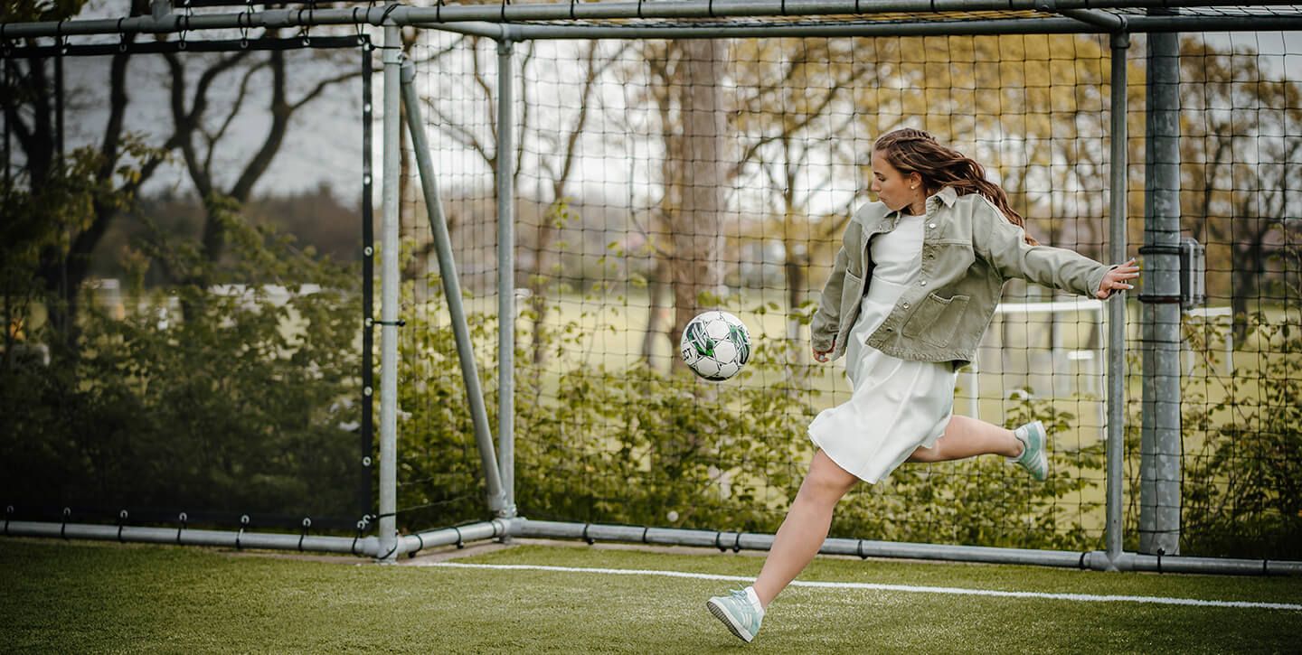 Fotograf i Hjørring – naturligt konfirmationsportræt af pige med fodbold på udendørs bane.