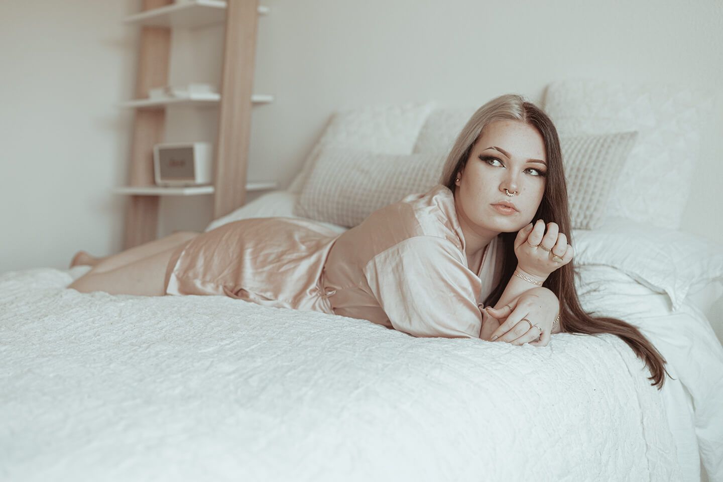 Boudoirfotografering i Aalborg – kvinde i lys silke-natkjole på seng, blødt lys og feminin ro.