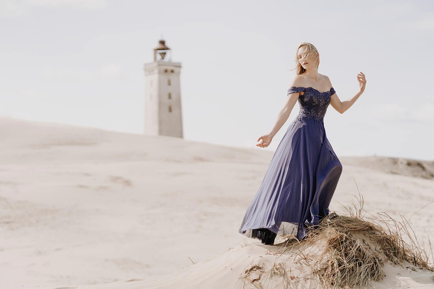 Model i lilla kjole foran Rubjerg Knude Fyr – æstetisk portræt i det nordjyske klitlandskab.