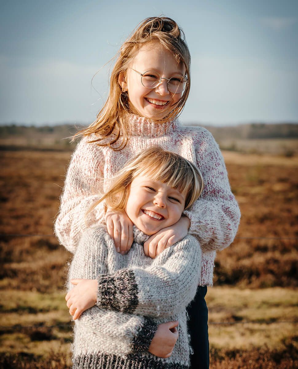 Naturlig børnefotografering i Aalborg – søskende der krammer med smil og nærvær i varmt lys.