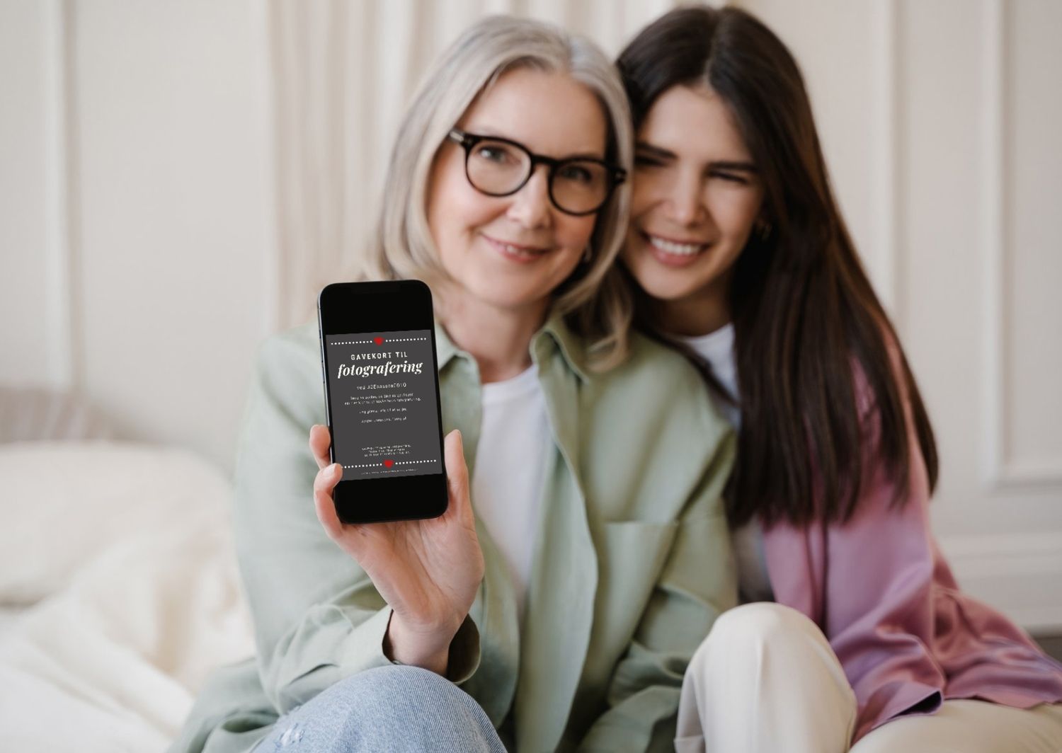 Mor og datter sidder med en mobiltelefon, med et gavekort fra fotograf i Aalborg.
