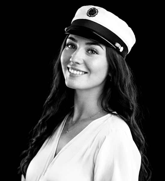 Sort-hvid studentportræt i studie – smilende ung kvinde med studenterhue fotograferet mod mørk baggrund i Aalborg.