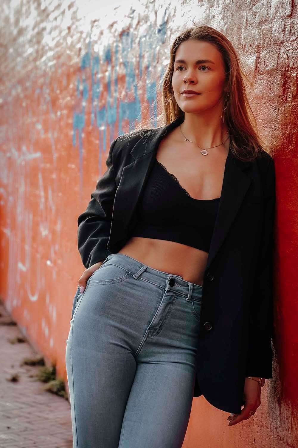Model læner sig mod rød væg med blå graffiti – urban modelfotografi i Aalborg.
