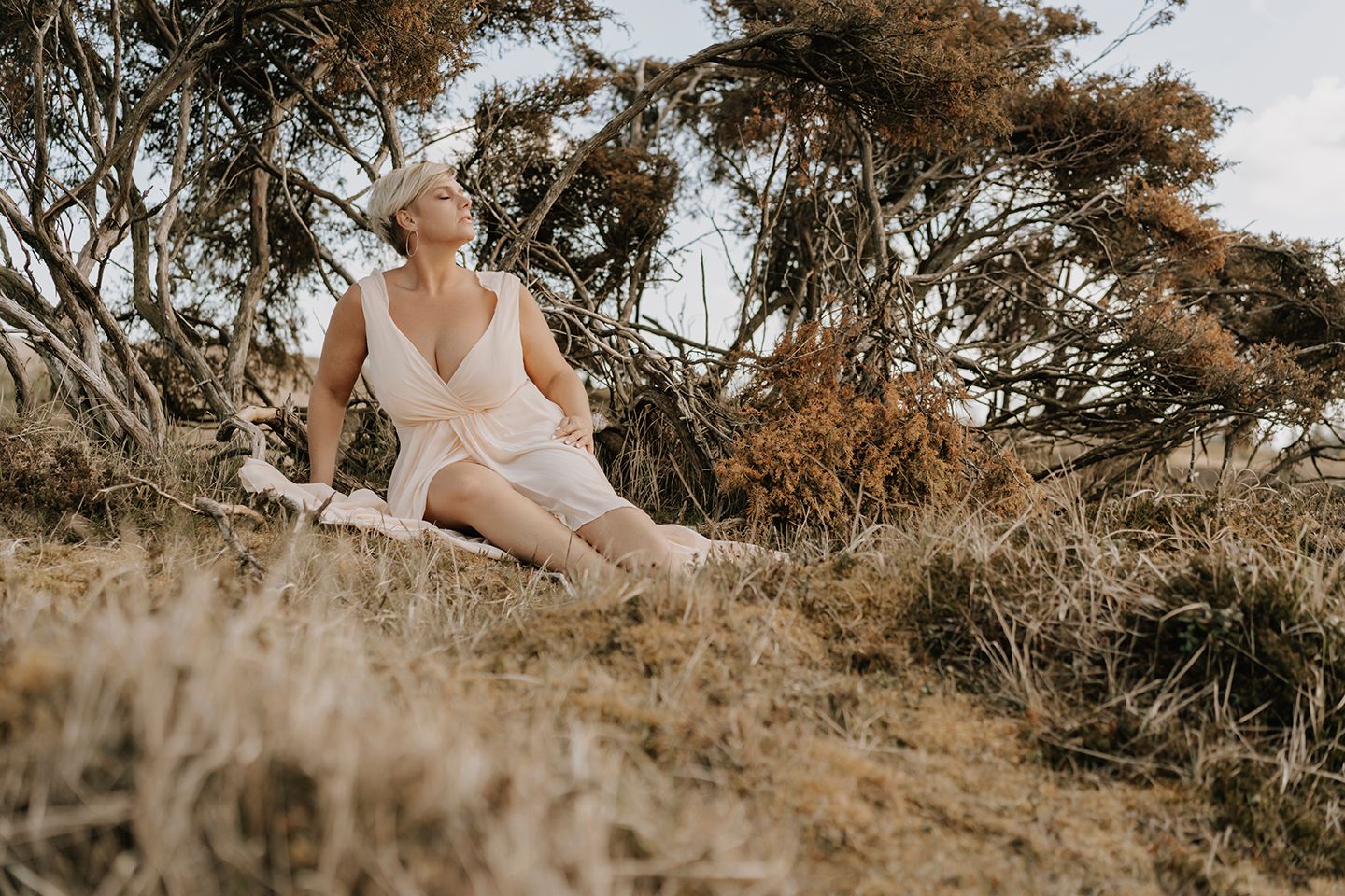Kvinde sidder i lyngen iført lys kjole – sensuelt outdoor-portræt fotograferet i Nordjylland.