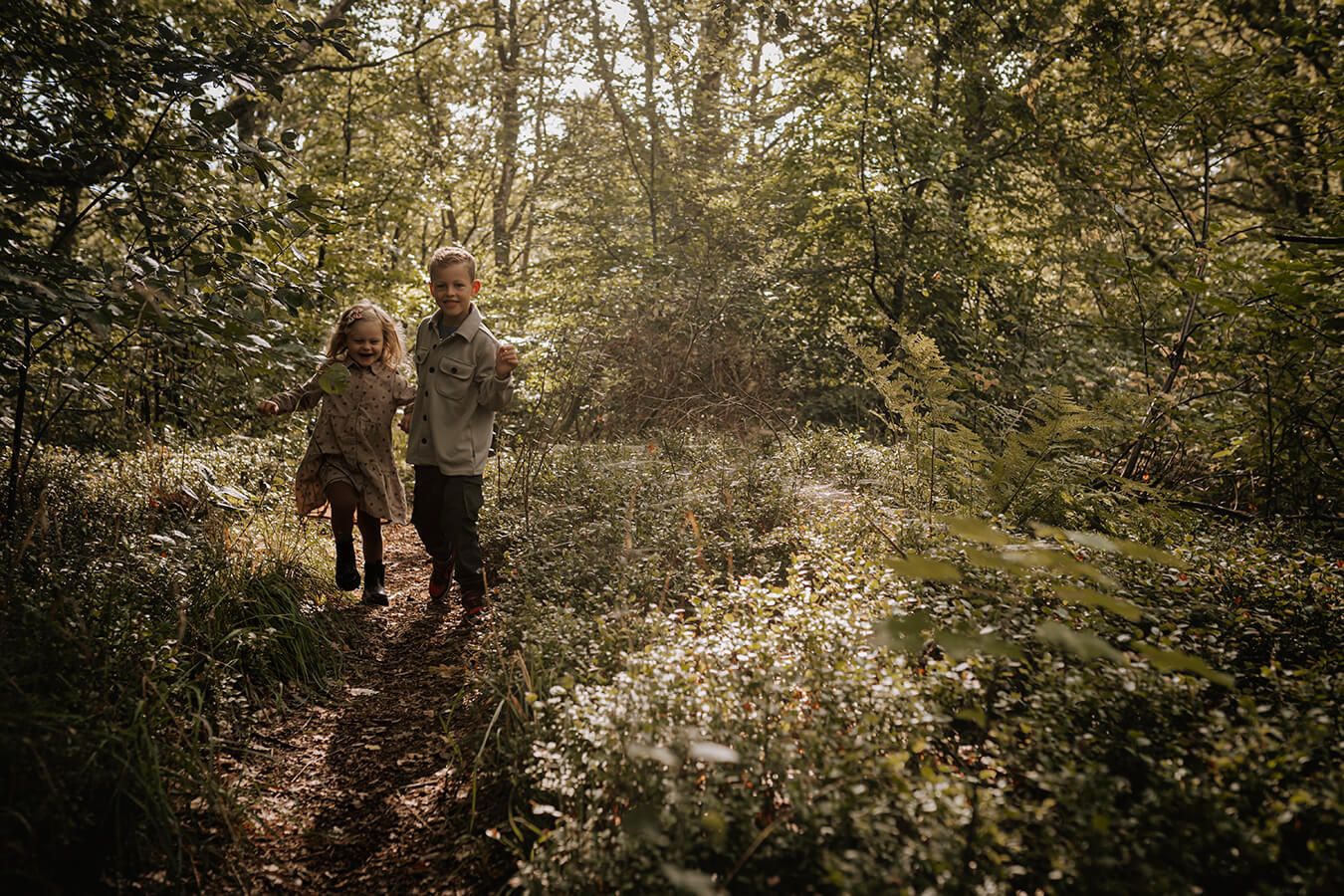 To børn løber sammen gennem skoven i naturligt lys – afslappet børnefotografering i Aalborg.