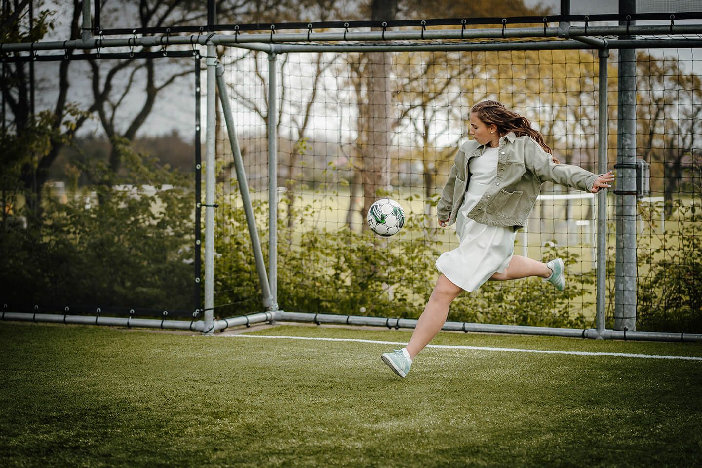 Konfirmationsbillede af konfirmand i kjole og sneakers, der spiller fodbold under fotografering i Nordjylland.