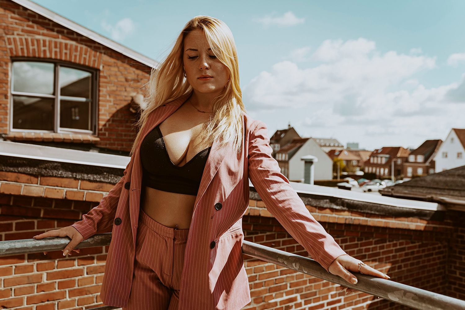 Modelfotografi i Aalborg – kvinde i rosa jakkesæt og sort top på bytag med stærkt udtryk.