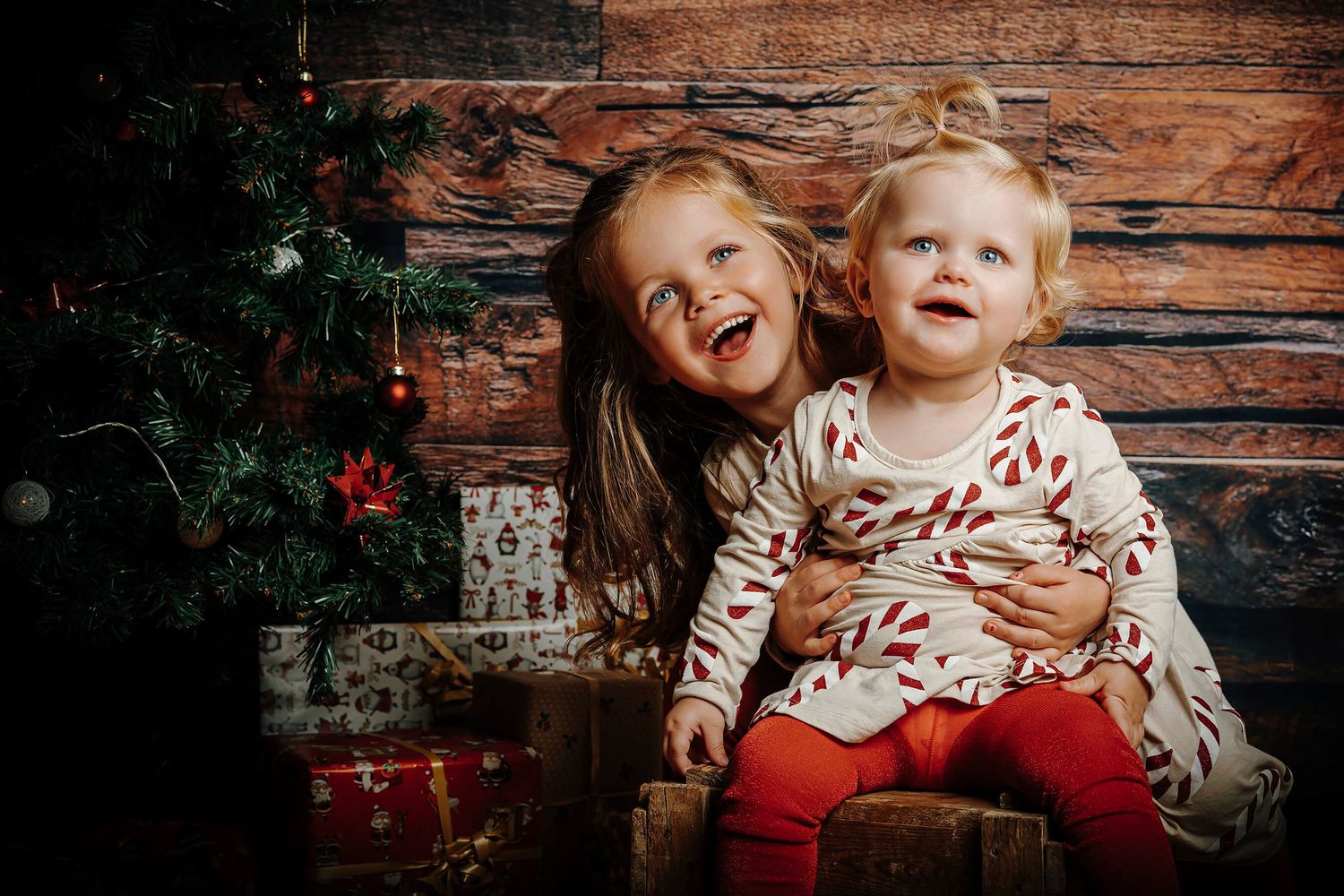 To glade søstre foran juletræ og julegaver ved julefotografering i Aalborg.