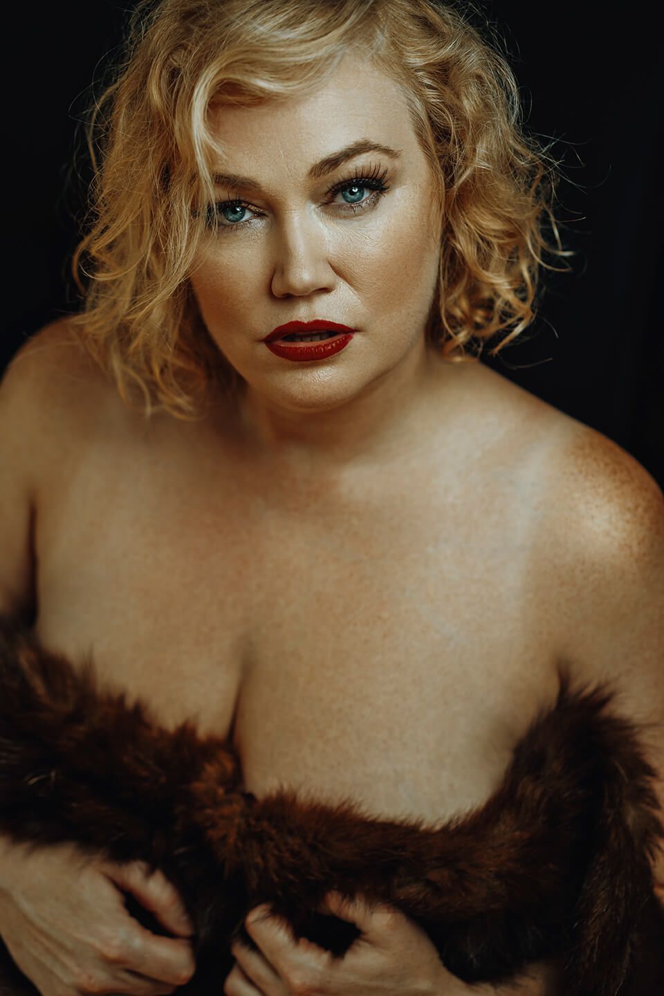 Boudoirfotografering i Aalborg – glamour close-up med rød læbestift og blød pelsdetalje mod mørk baggrund.