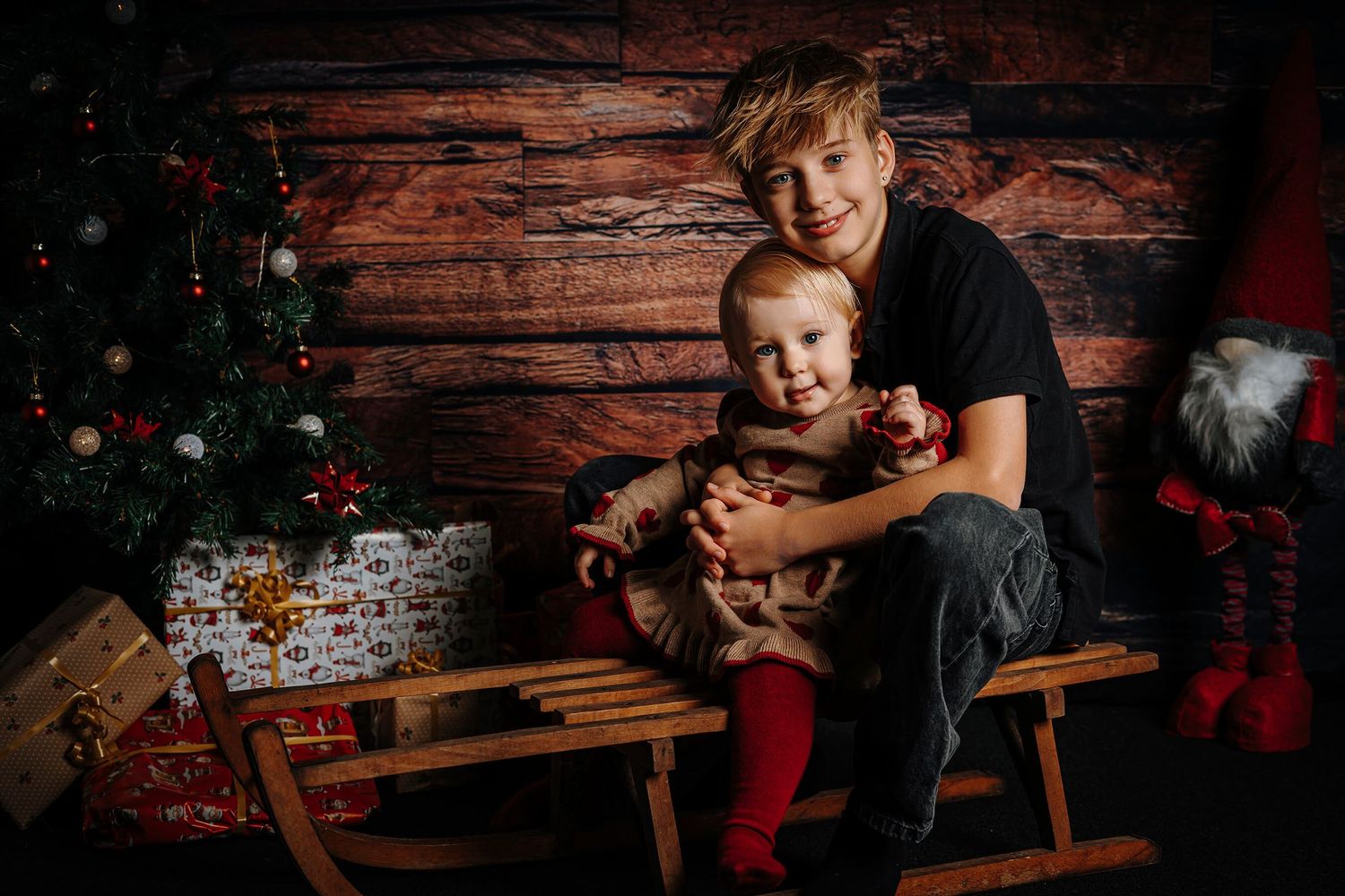 Større søskende holder baby på slæde i stemningsfuldt julemiljø.