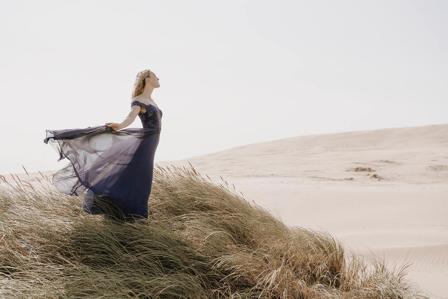 Model i lilla kjole står i vinden på toppen af en klit – fotograferet i Nordjylland af modelfotograf