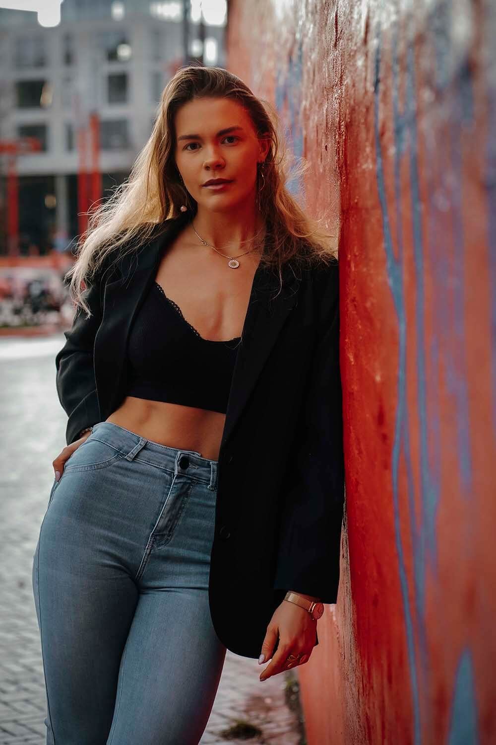Kvinde i sort blæser og crop top – stående mod byvæg i kreativt fotoshoot i Aalborg.