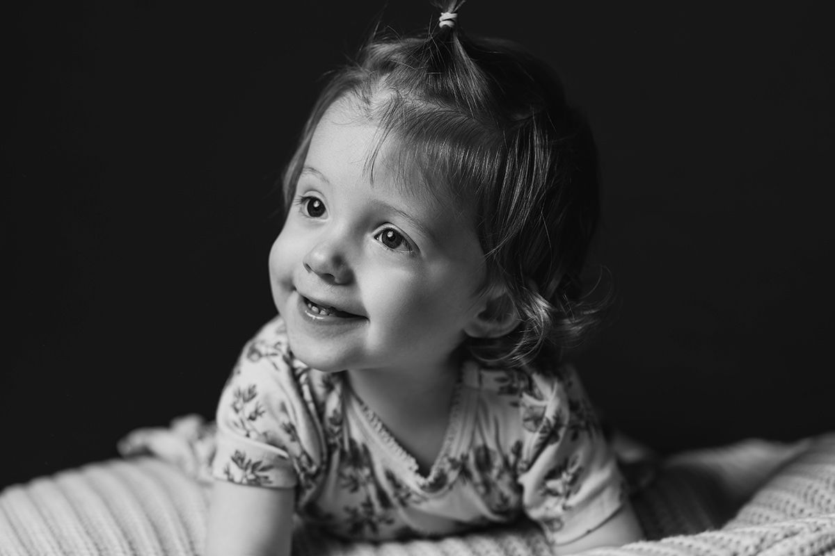 Familiefotograf i Aalborg & Nordjylland har taget et billede af en meget lille og glad pige, der ligger på en pude.