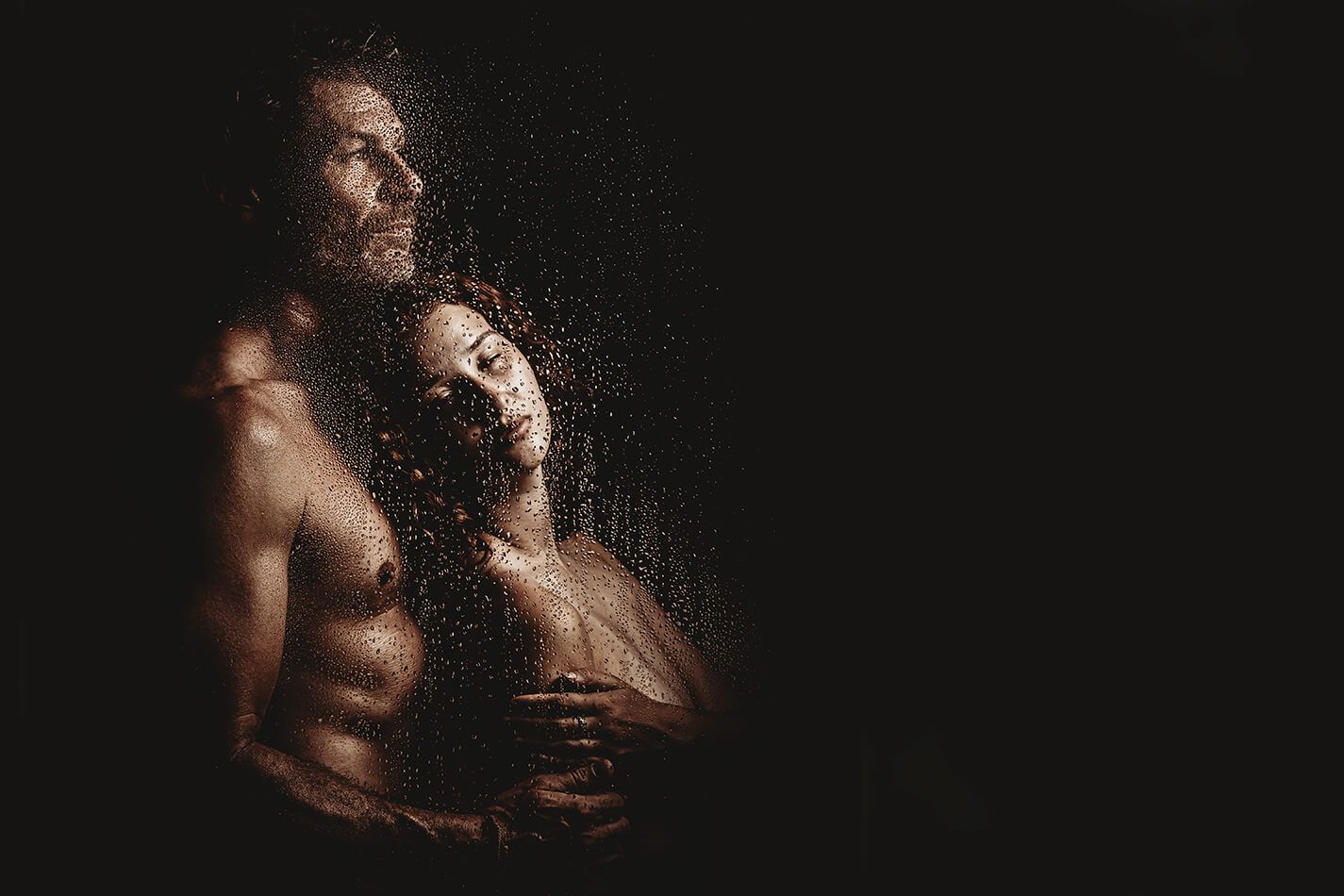 Intim parfotografering bag vådt glas med mørk stemning og æstetisk boudoirudtryk.