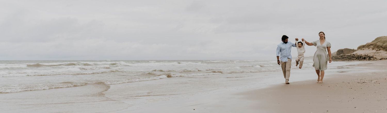 Familie går langs stranden med deres barn – naturlig familiefotografering ved havet nær Aalborg, JOEhansenFOTO.