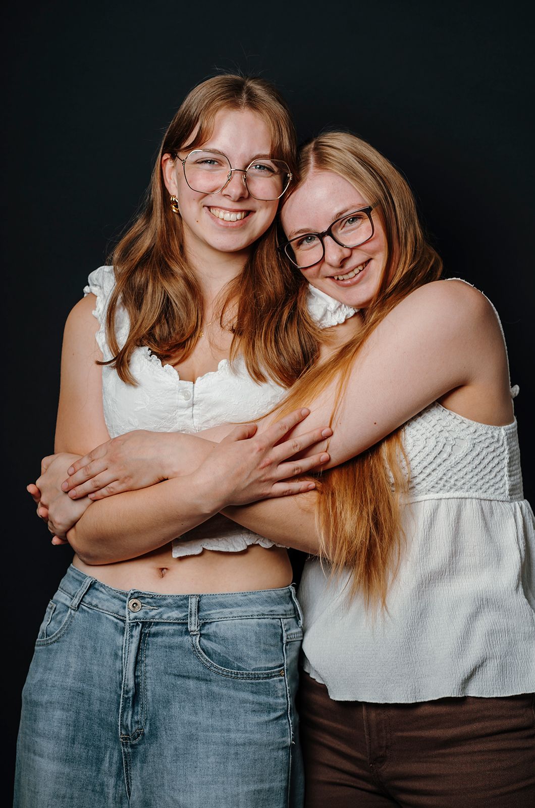 Familiefotografering i Aalborg – naturligt og kærligt portræt af to unge kvinder, der omfavner hinanden foran en mørk baggrund.